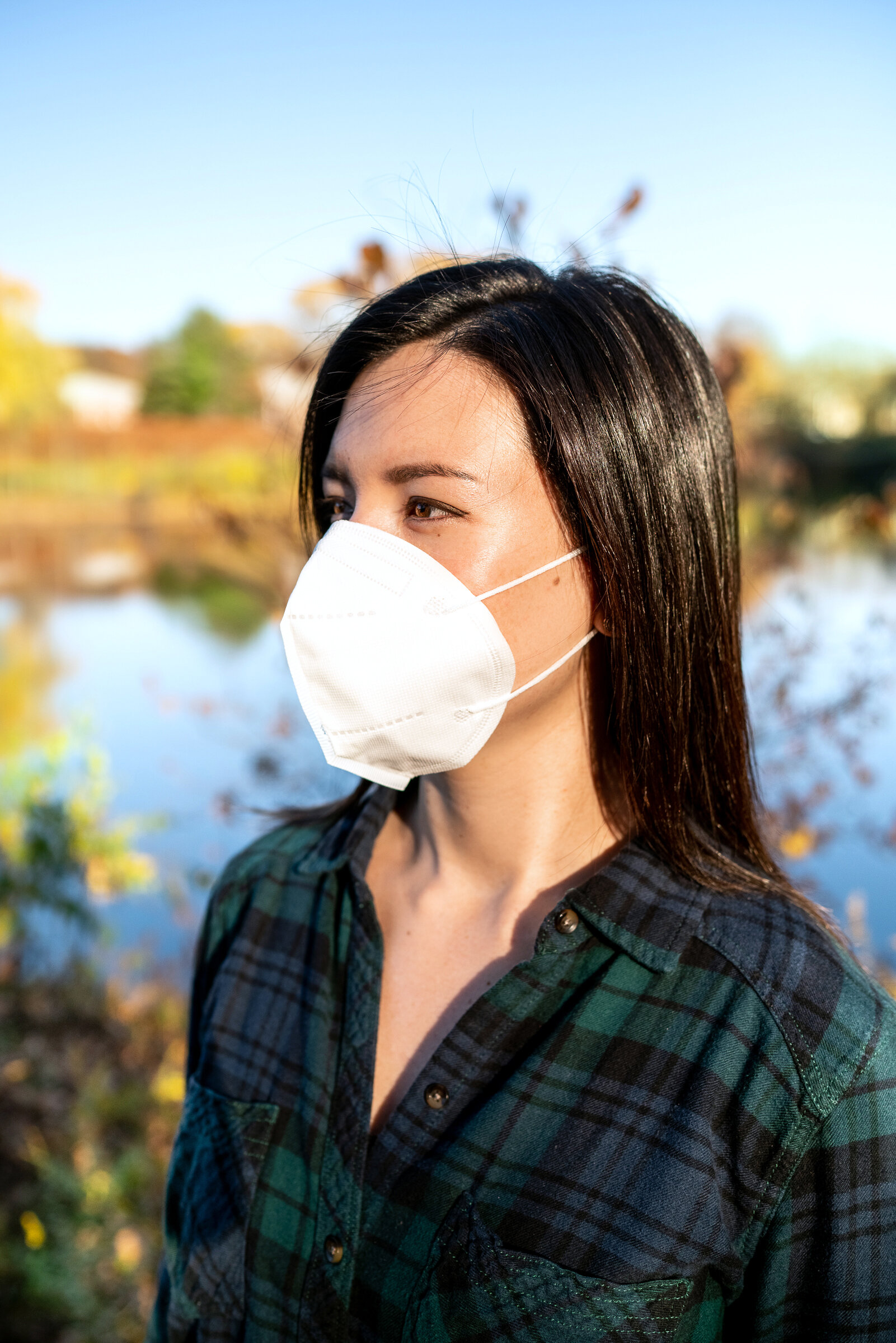 A woman standing near a river wearing a mask