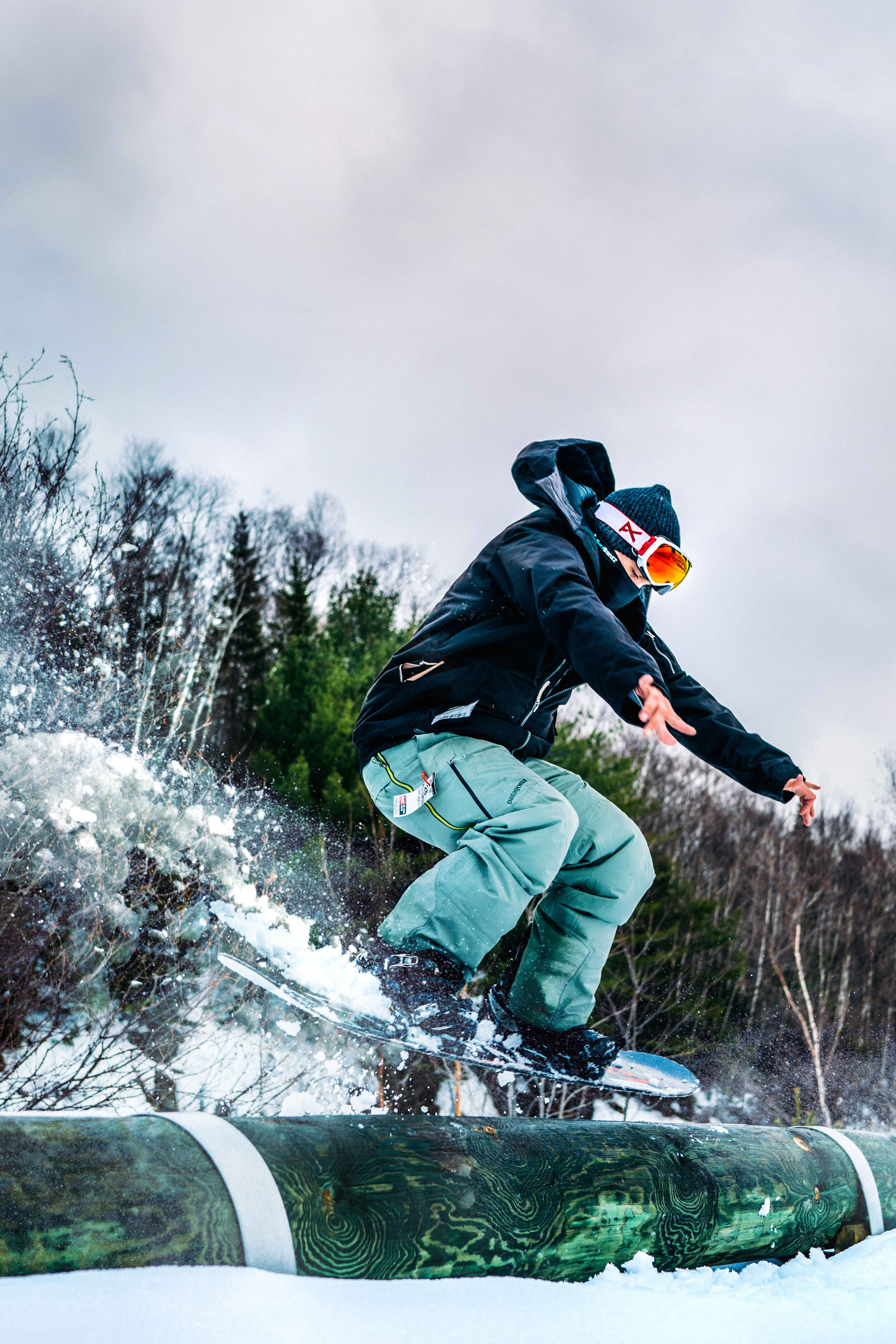 A masked snowboarder jumping a log