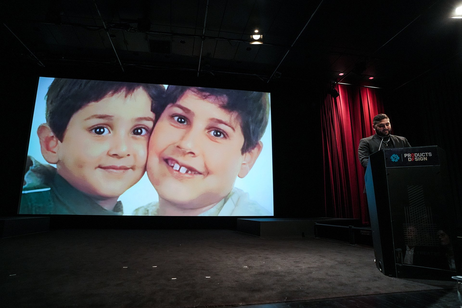  Speaker at the podium with image projected on screen of the faces of two children 