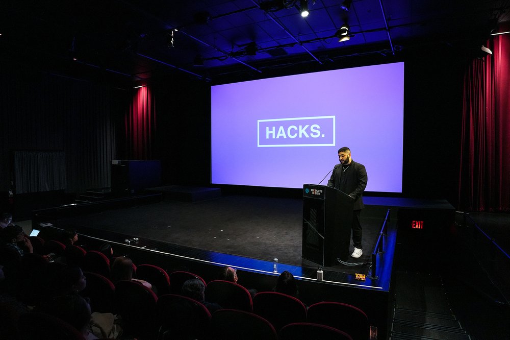  Speaker at podium with screen behind featuring a purple image that reads “HACKS” 