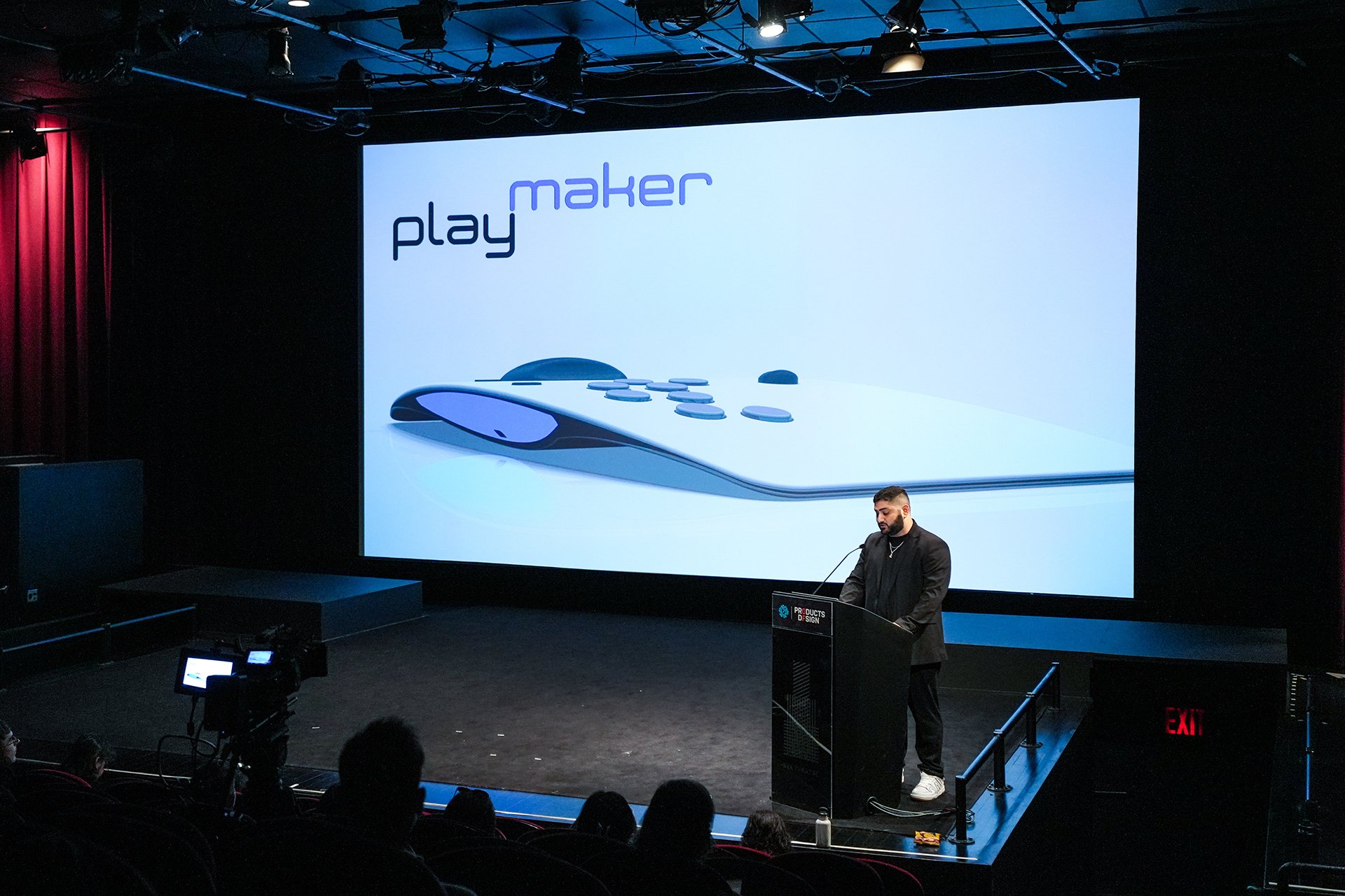  Speaker at podium with screen behind featuring a image of a product that reads “Play Maker” 