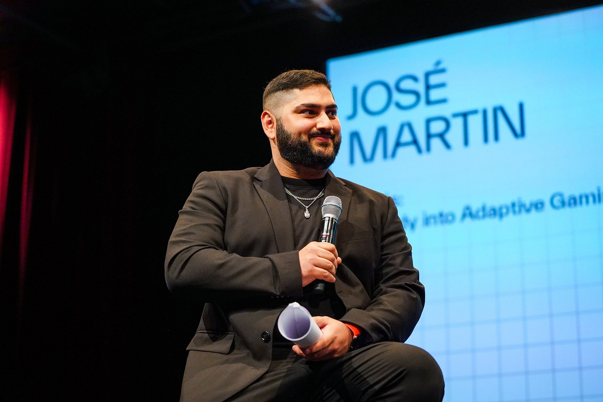  Speaker with microphone on the stage with name “JOSE MARTIN” projected behind him on the screen 