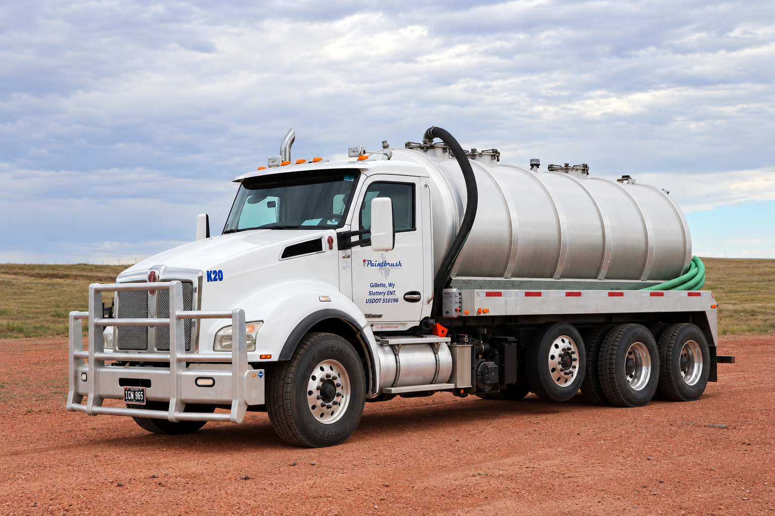 A white water tanker truck parked on a dirt ground with an open field and cloudy sky in the background.