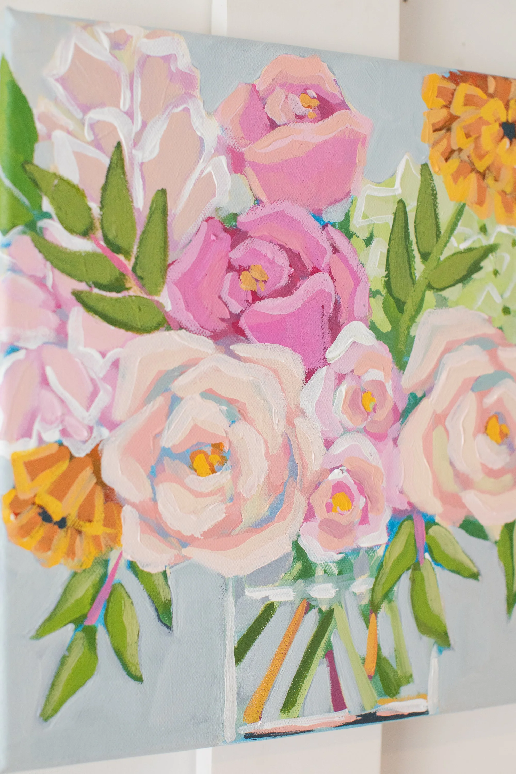 A colorful painting of a bouquet of pink and peach roses with green leaves in a clear glass vase, accented with yellow and orange flowers.