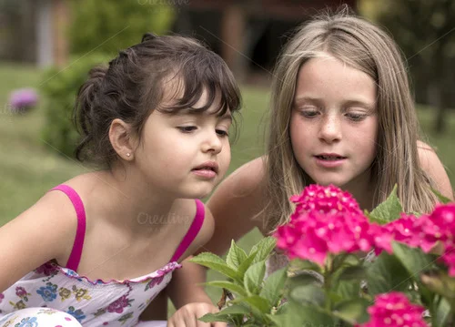Two girls looking into a flower bush.
