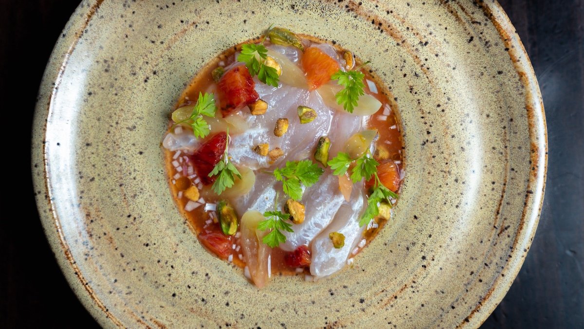 A plate of ceviche garnished with fresh cilantro, chopped pistachios, and diced tomatoes.
