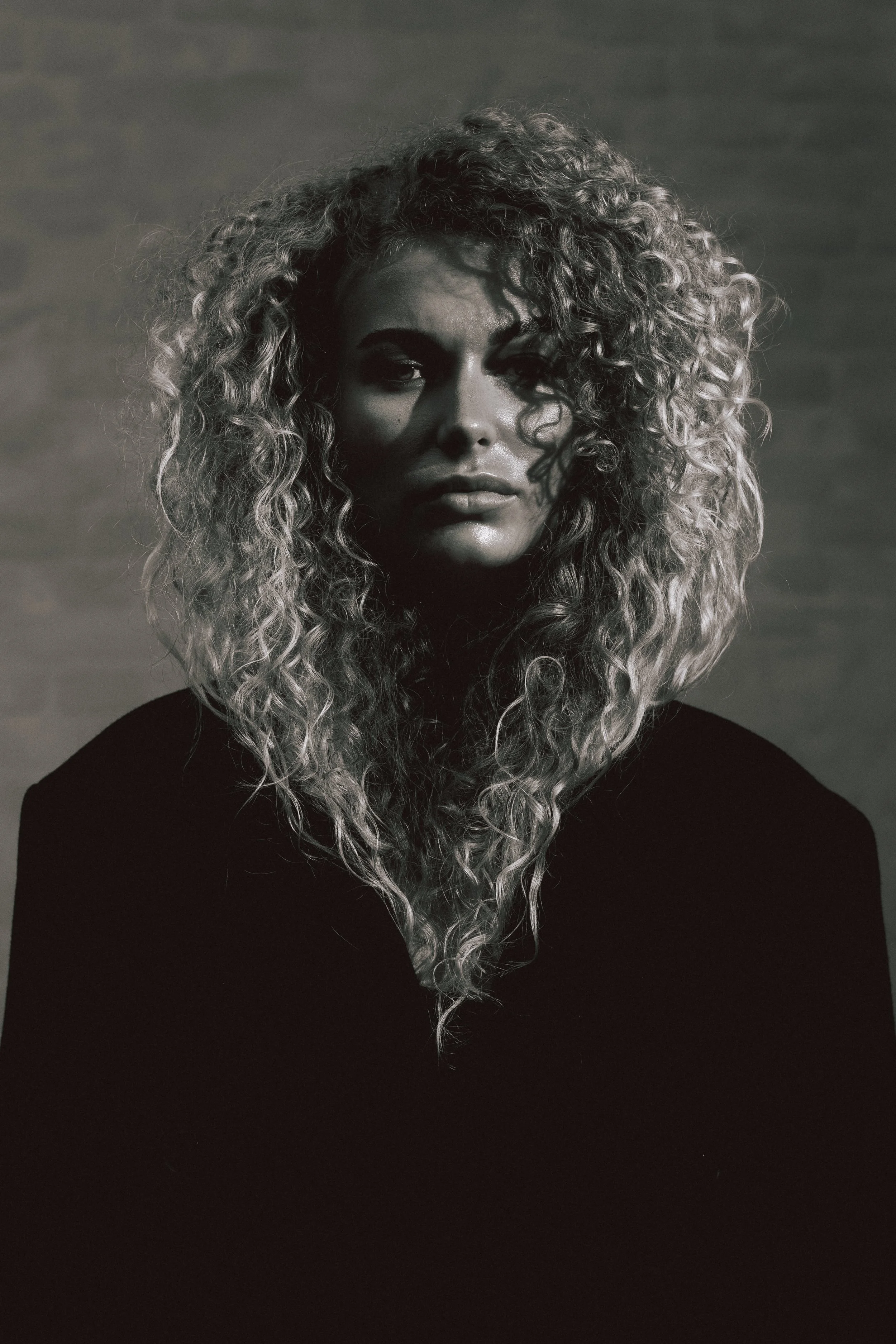 Black-and-white portrait of a woman with long, curly hair looking directly at the camera.