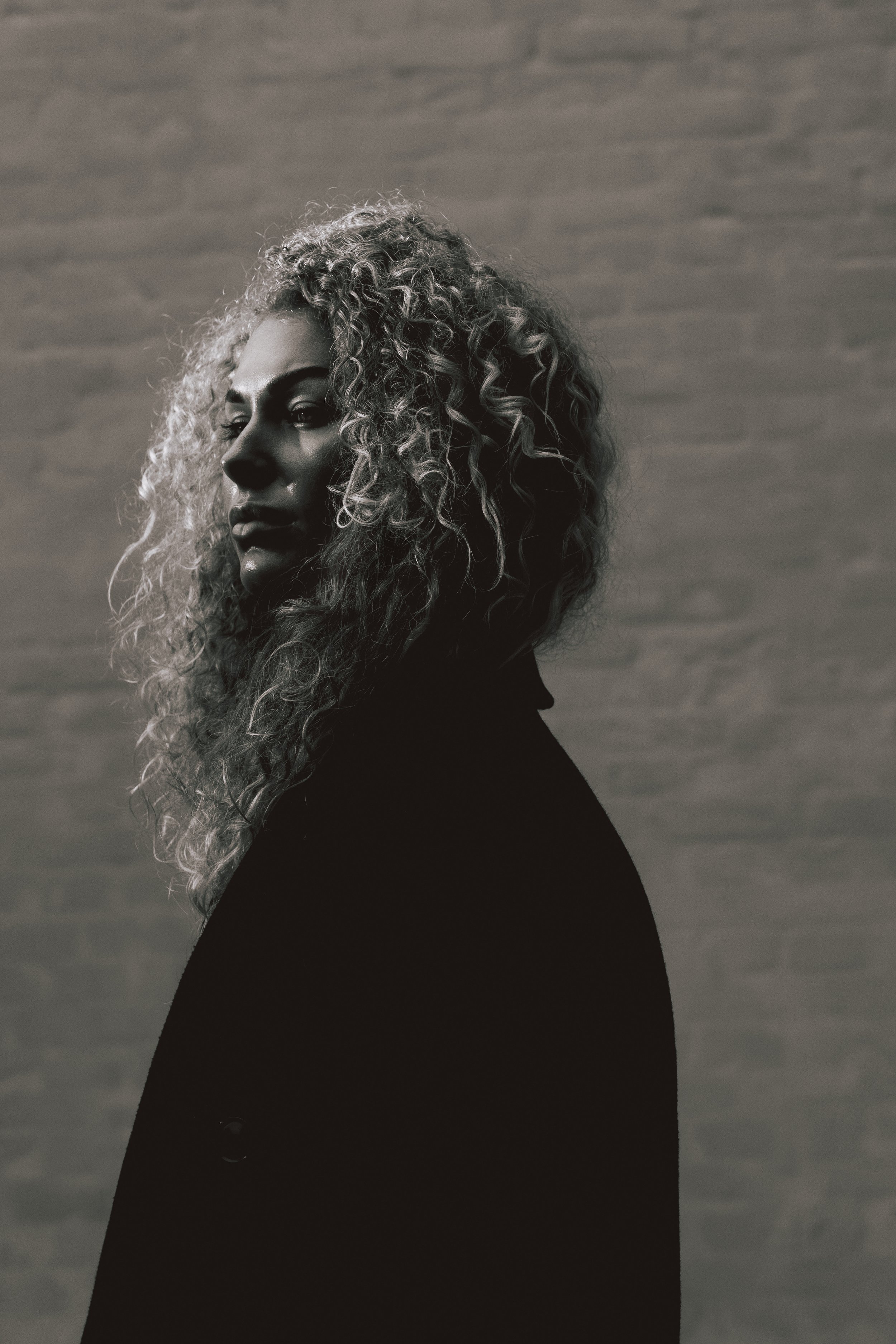 A black and white photo of a woman with curly hair standing against a textured background.