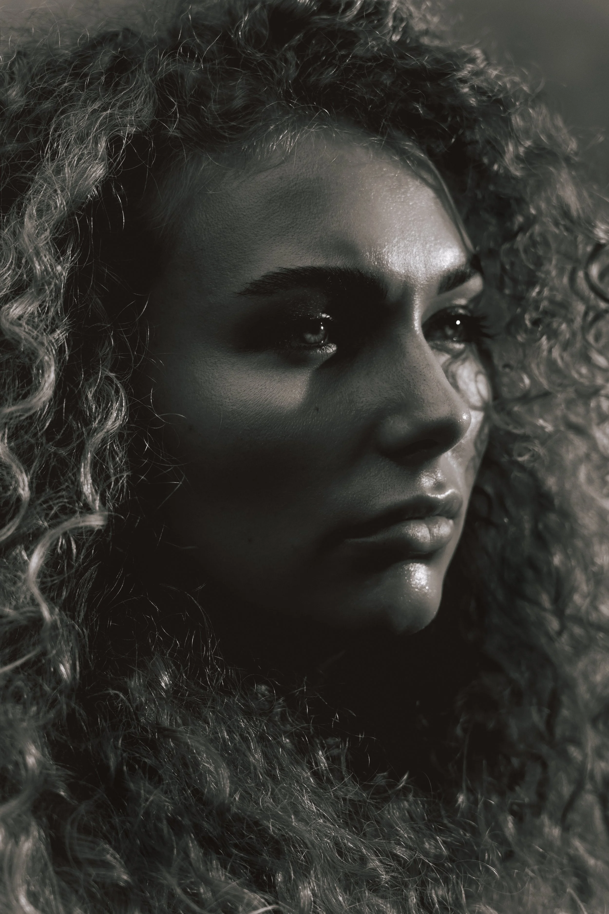 Close-up photo of a woman's face with curly hair, showing her forehead, eyes, nose, and lips in monochrome.