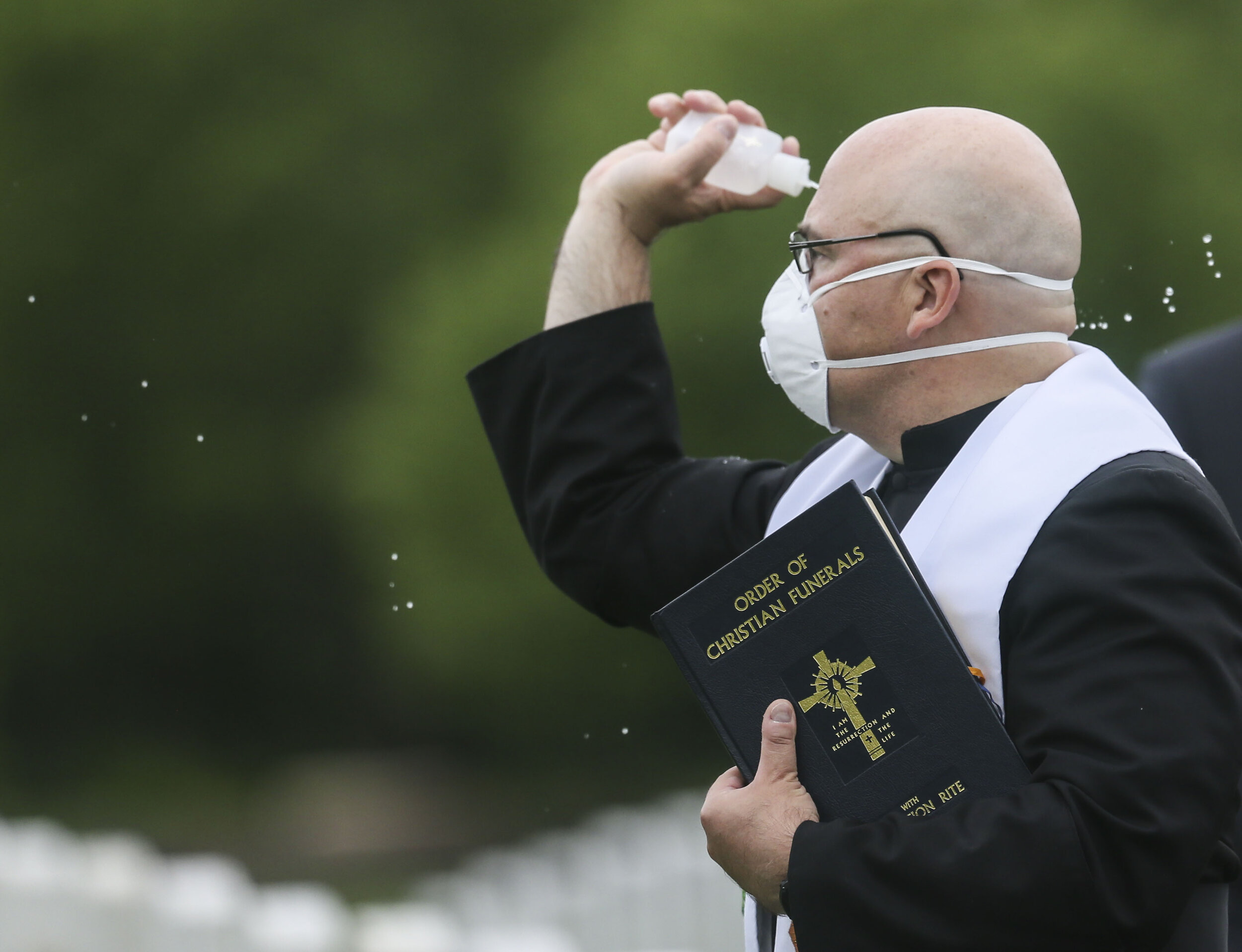  Father Antonio Dittmer throws holy water near the burial sight of Roberto Antu,where his limited family members gather at the Rock Island National Cemetery, Thursday May 21, 2020.  
