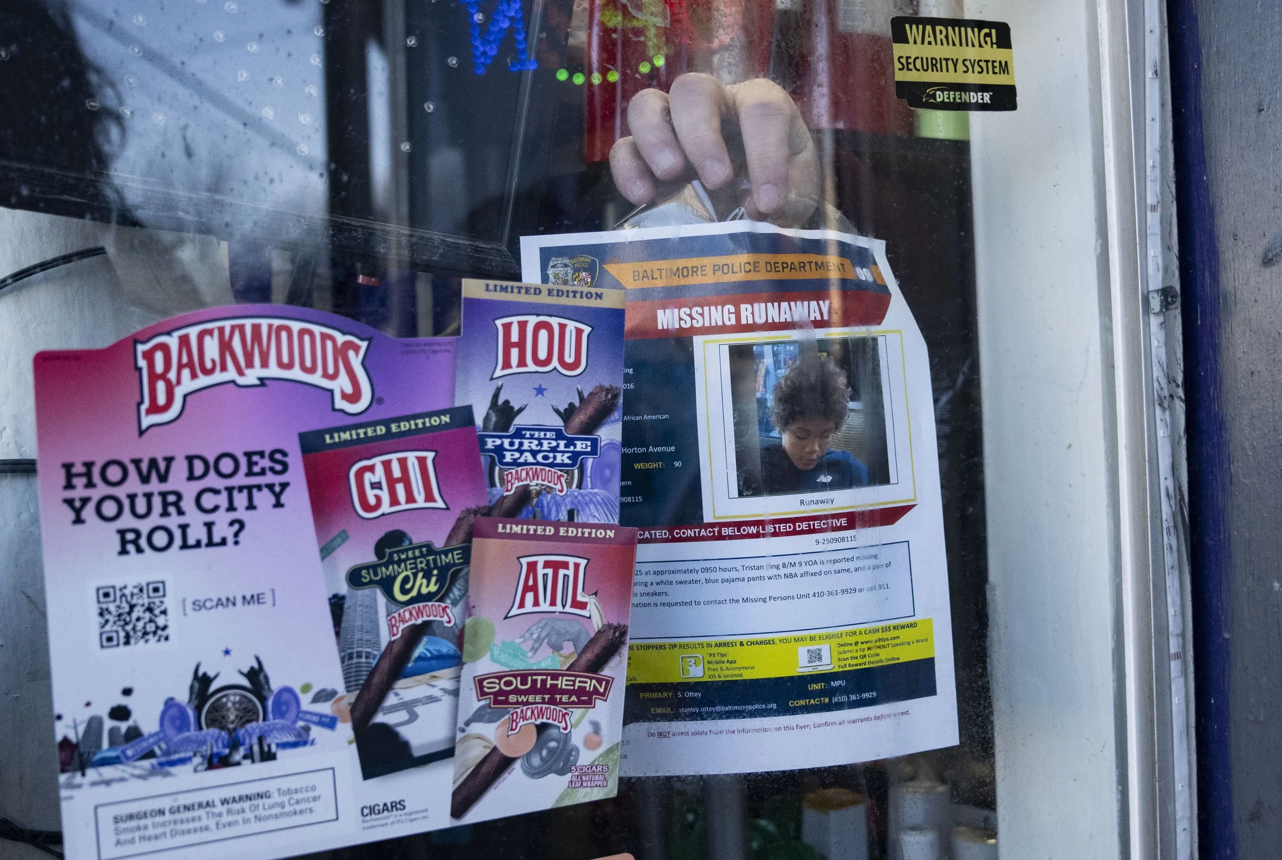  Scott tapes a missing poster in a corner store window. People who shop there said they’ve seen Tristan recently. 