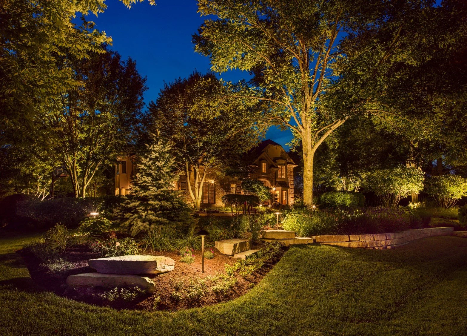 Outdoor landscape lighting illuminating trees and garden beds around a home