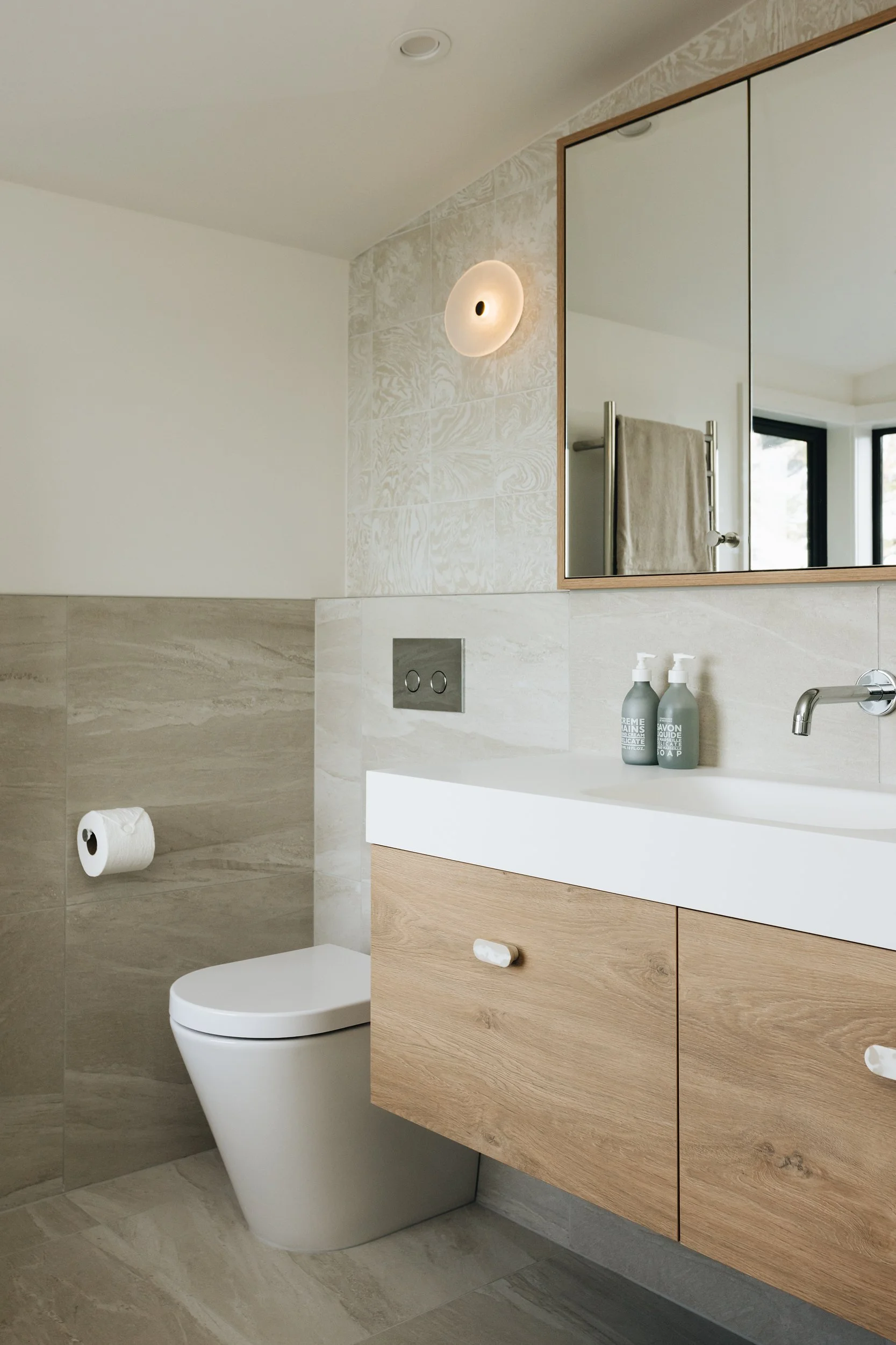 Neutral toned bathroom with Variegati Avorio tiles and timber cabinetry featuring custom coloured resin handles from The Arc Dept
