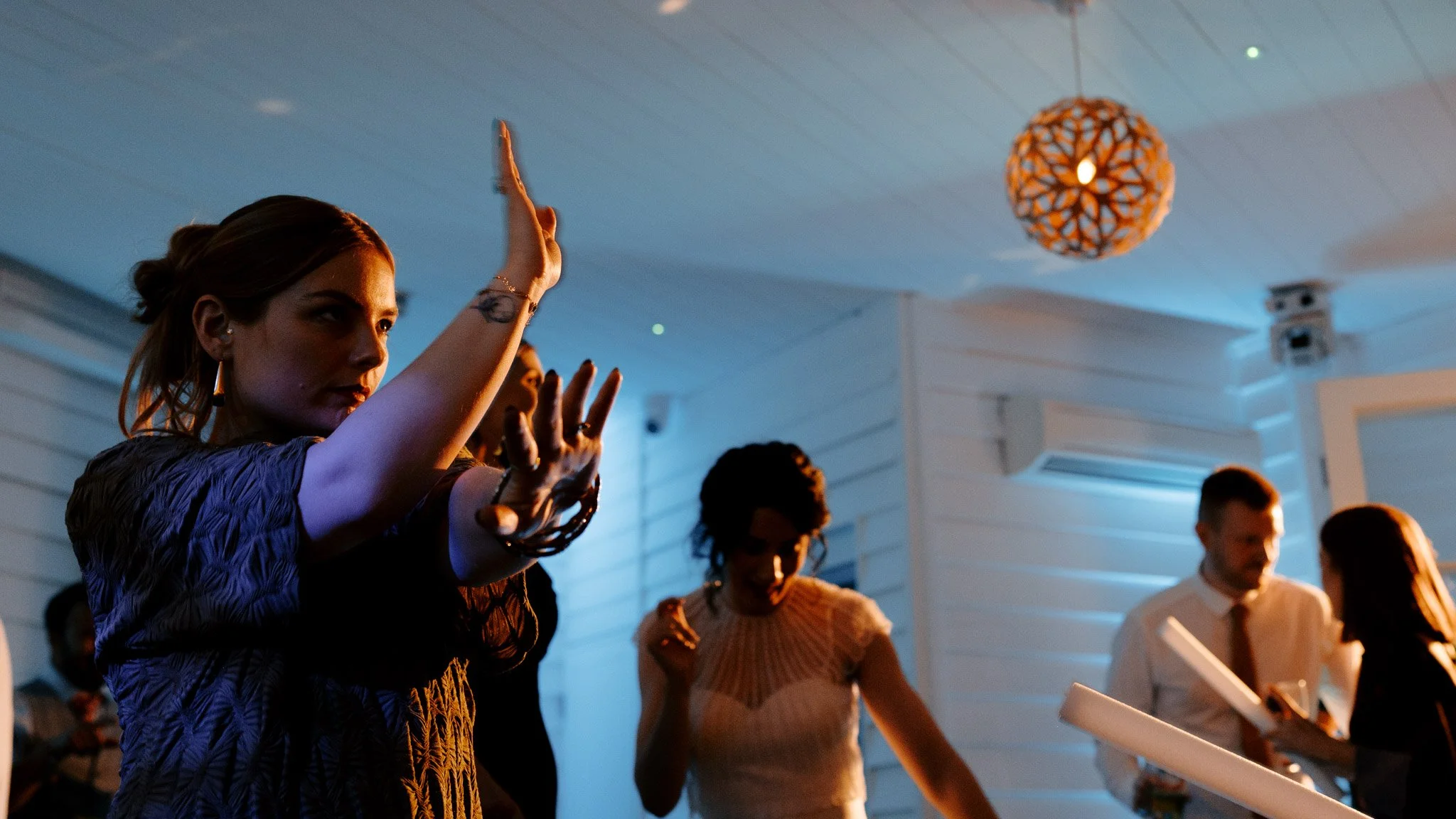 People dancing at a party with white walls and a geometric hanging light fixture.