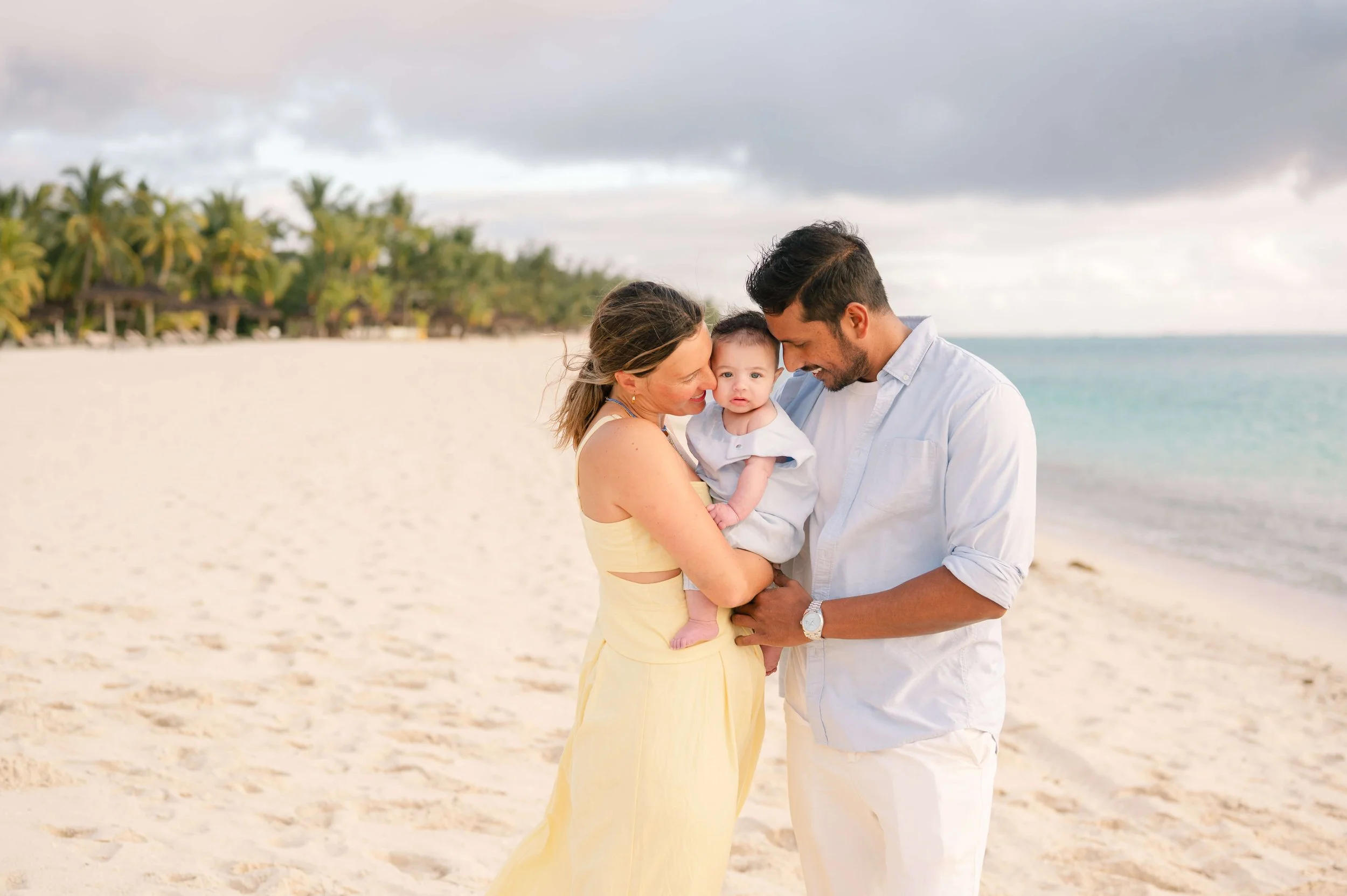 Parents cuddling baby on a palm tree lined beach in Mauritius