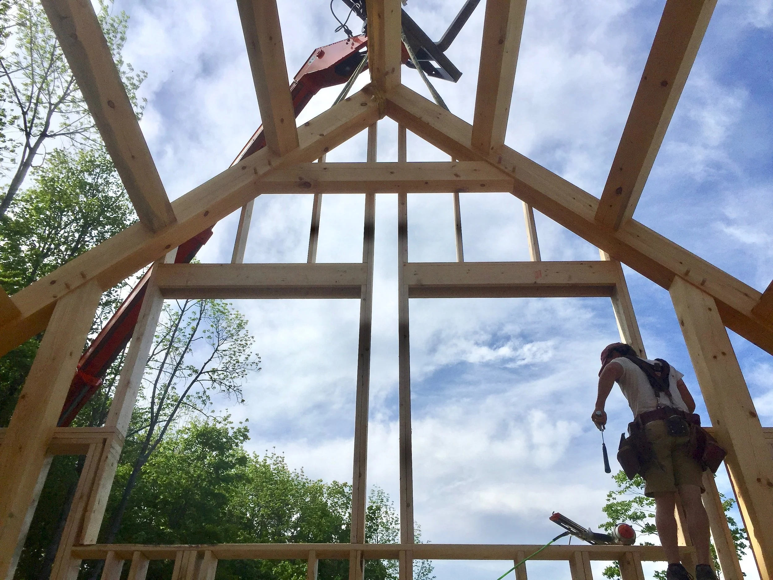 Construction worker standing inside the wooden framework of a building under construction, with a crane or lift above. Construction by Corrigan & Klein Artisan Builders.