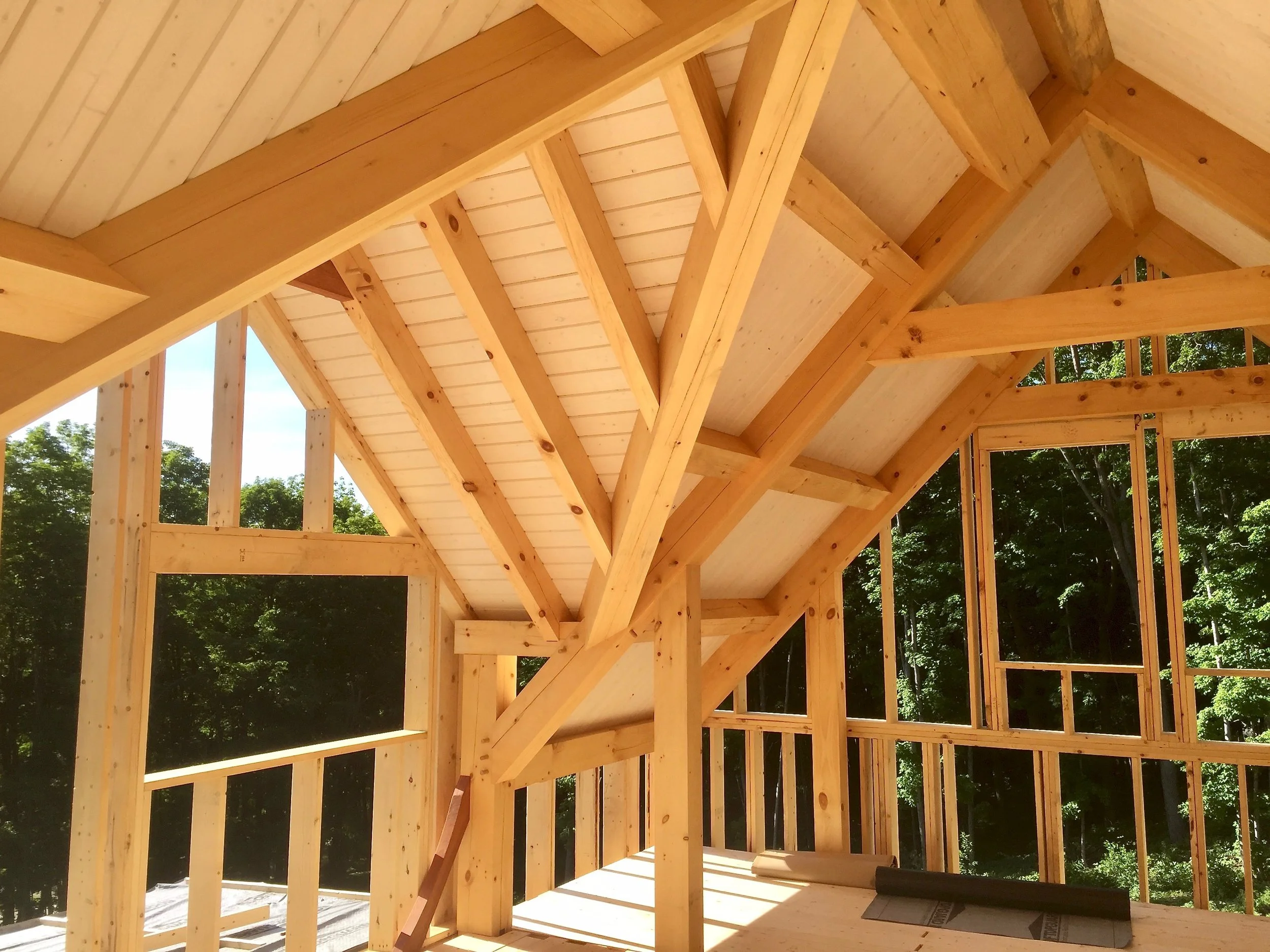 Inside view of a house under construction with exposed wooden framing and roof trusses. Construction by Corrigan & Klein Artisan Builders.