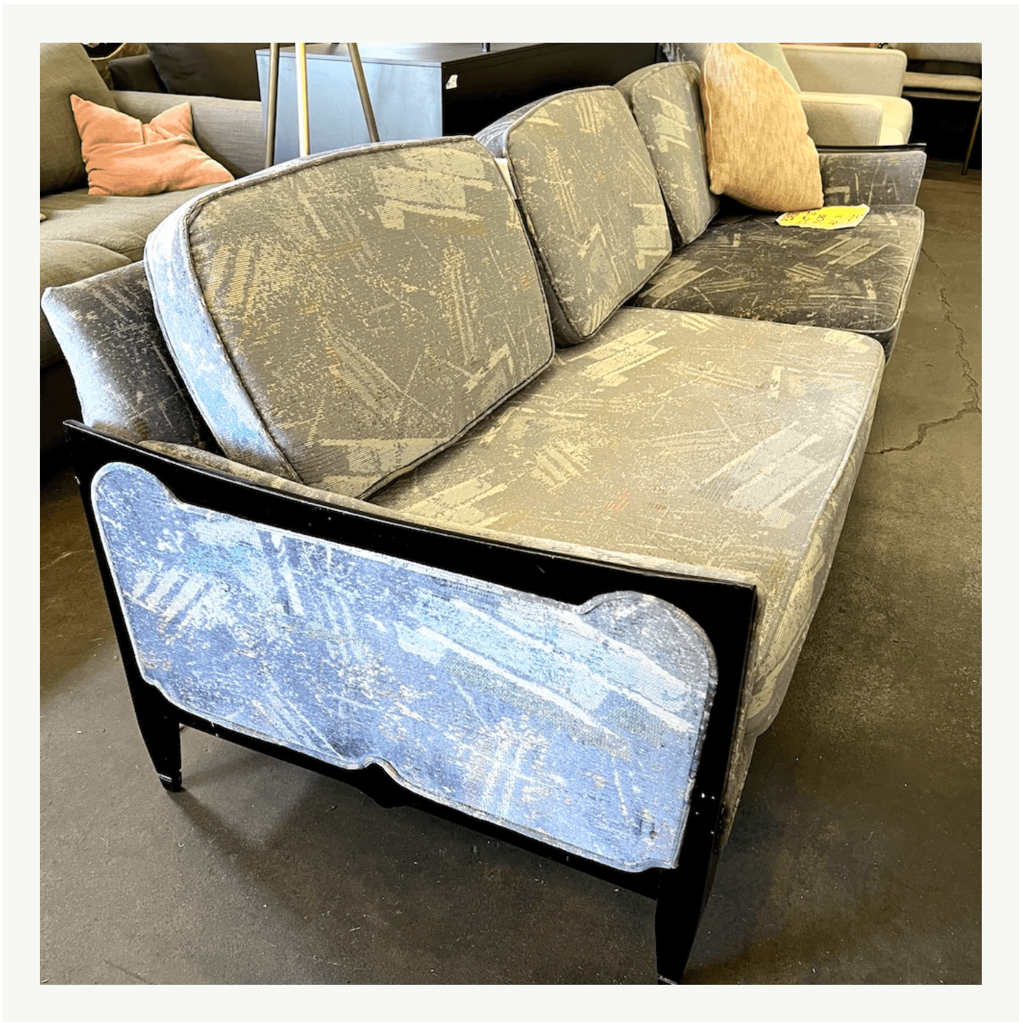 Vintage Hollywood Regency sofa with black lacquered frame and worn abstract upholstery at Poor Honey's Oakland — a reupholstery project with serious bones
