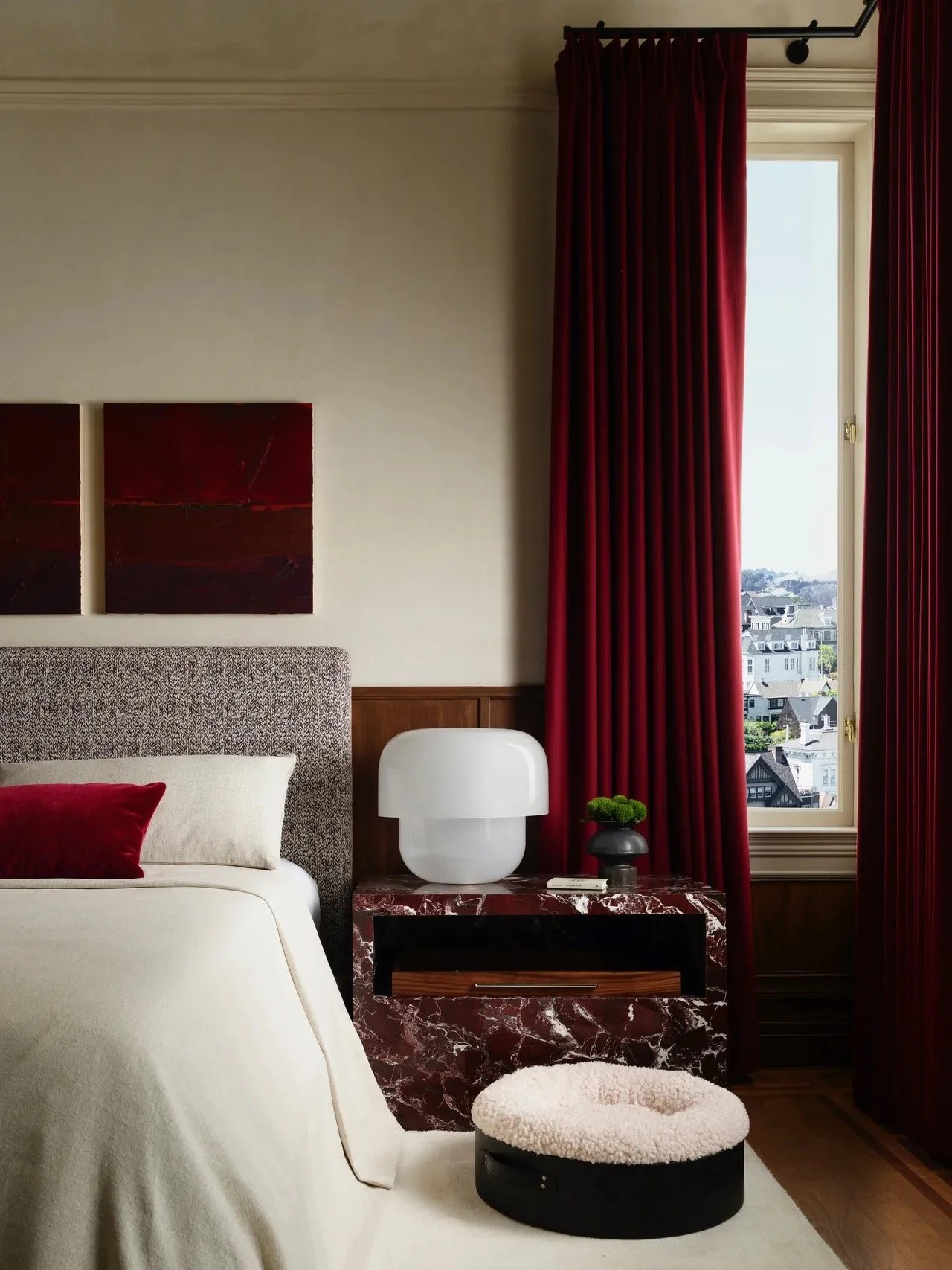 Close-up of reupholstered bed headboard in Rosemary Hallgarten Cachet in claret with natural linen pillows by Revitaliste , dark red marble nightstand, and crimson velvet drapery in Castellanos Interiors' West Red bedroom at the 2026 SF Showcase