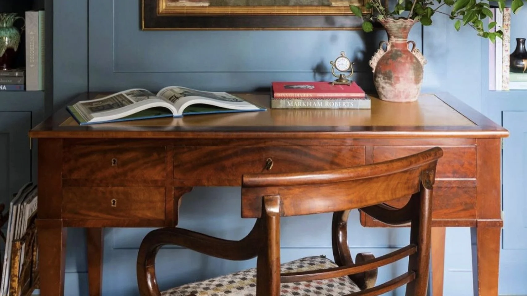 Wood dining table with blue upholstered chairs and brass candlesticks against dark blue paneled wall