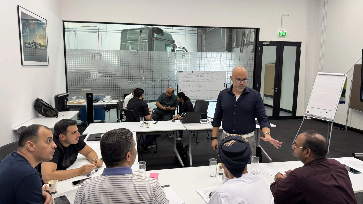 Coach H facilitating a discussion with participants around a workshop table