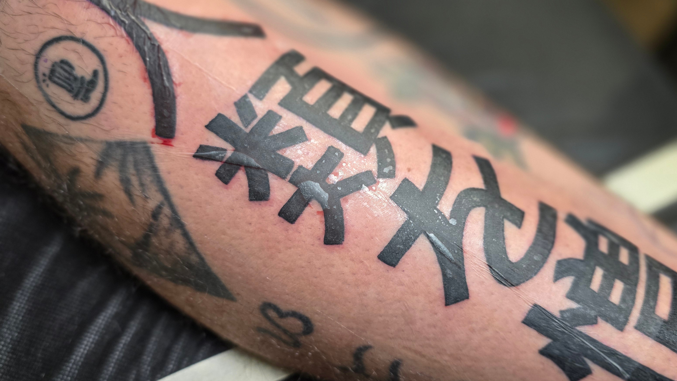A fresh tattoo protected by a clear medical-grade adhesive bandage, showing a normal amount of plasma and ink buildup (ink sac).