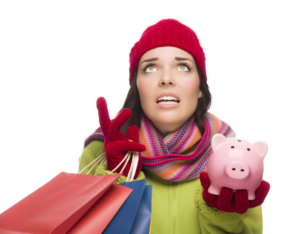Stressed Mixed Race Woman Wearing Winter Clothing Looking Up Holding Shopping Bags and Piggybank Isolated on White Background.