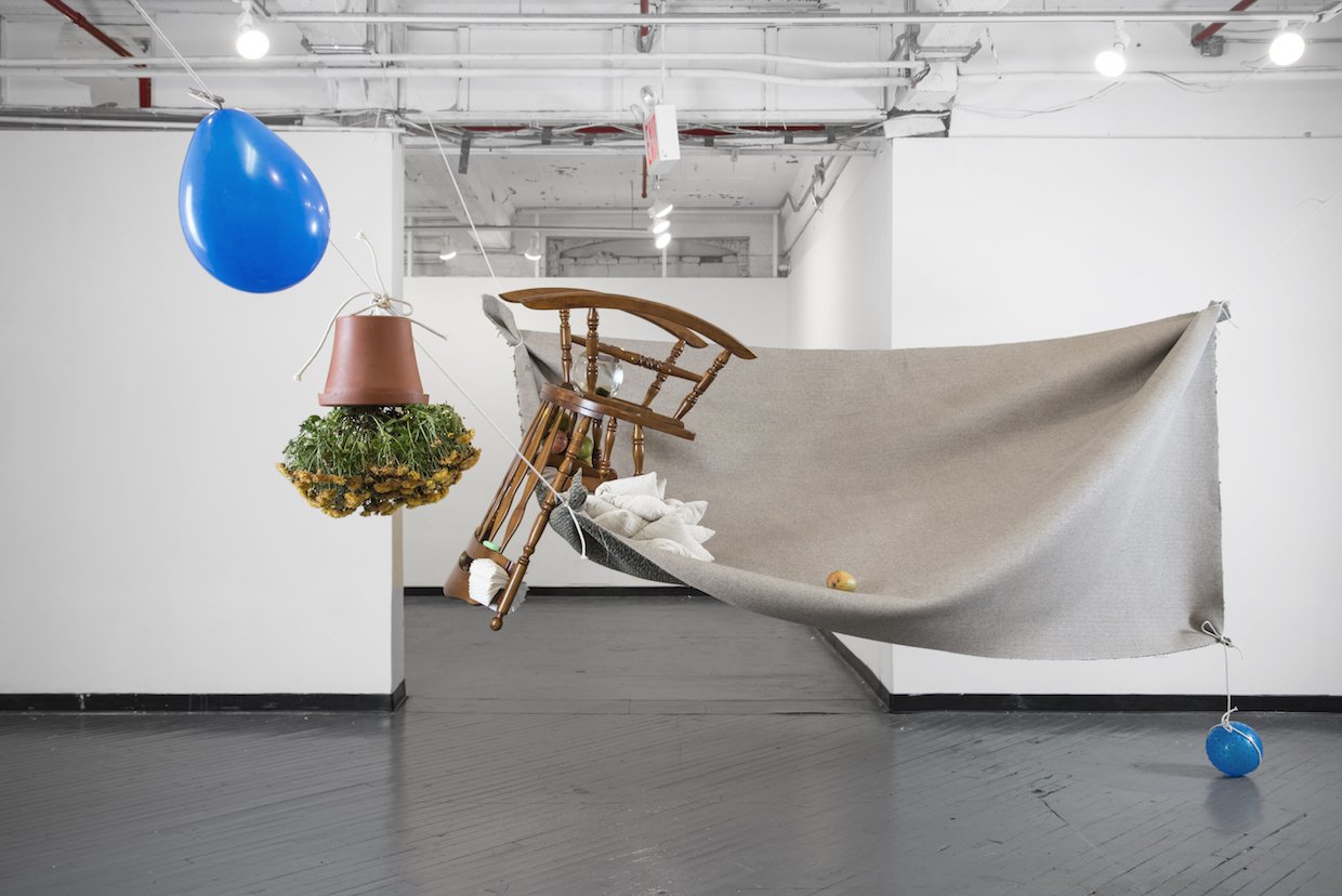   This May Fall (flying carpet) , 2014, 8 mangoes, yellow marigold flowerpot, blue balloon, 7’ x 12’ woven carpet, clothes line, clothes line clip, blue plastic ball, 4 white cushions, fish in a fishbowl with water and moss, napkins, green soap bar, 