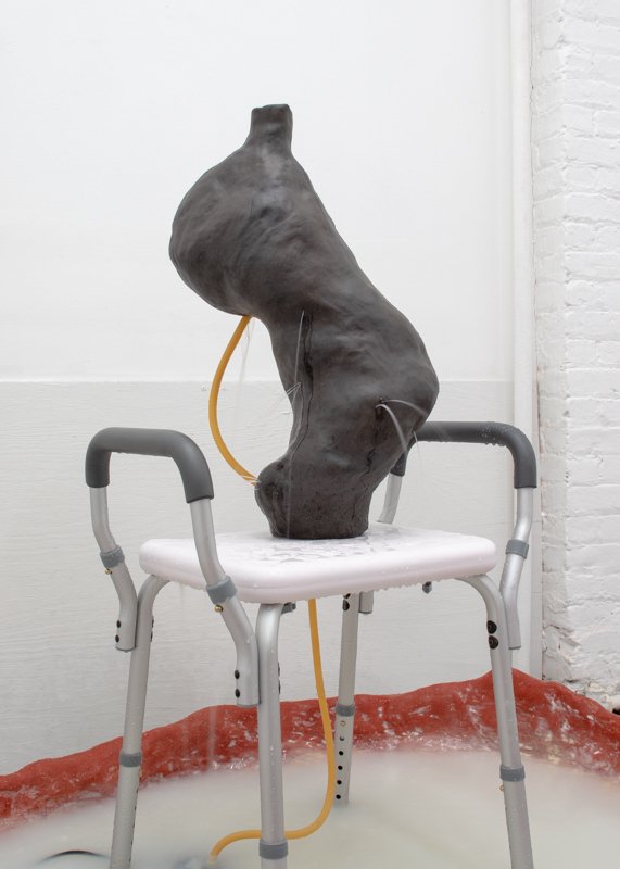   Out of the calf, into the mouth,  2021, 48" x 55" x 44", Ceramic stoneware, shower chair, fiberglass reinforced gypsum cement, wax, oil, latex tubing, fountain pump, water, oil of milk 