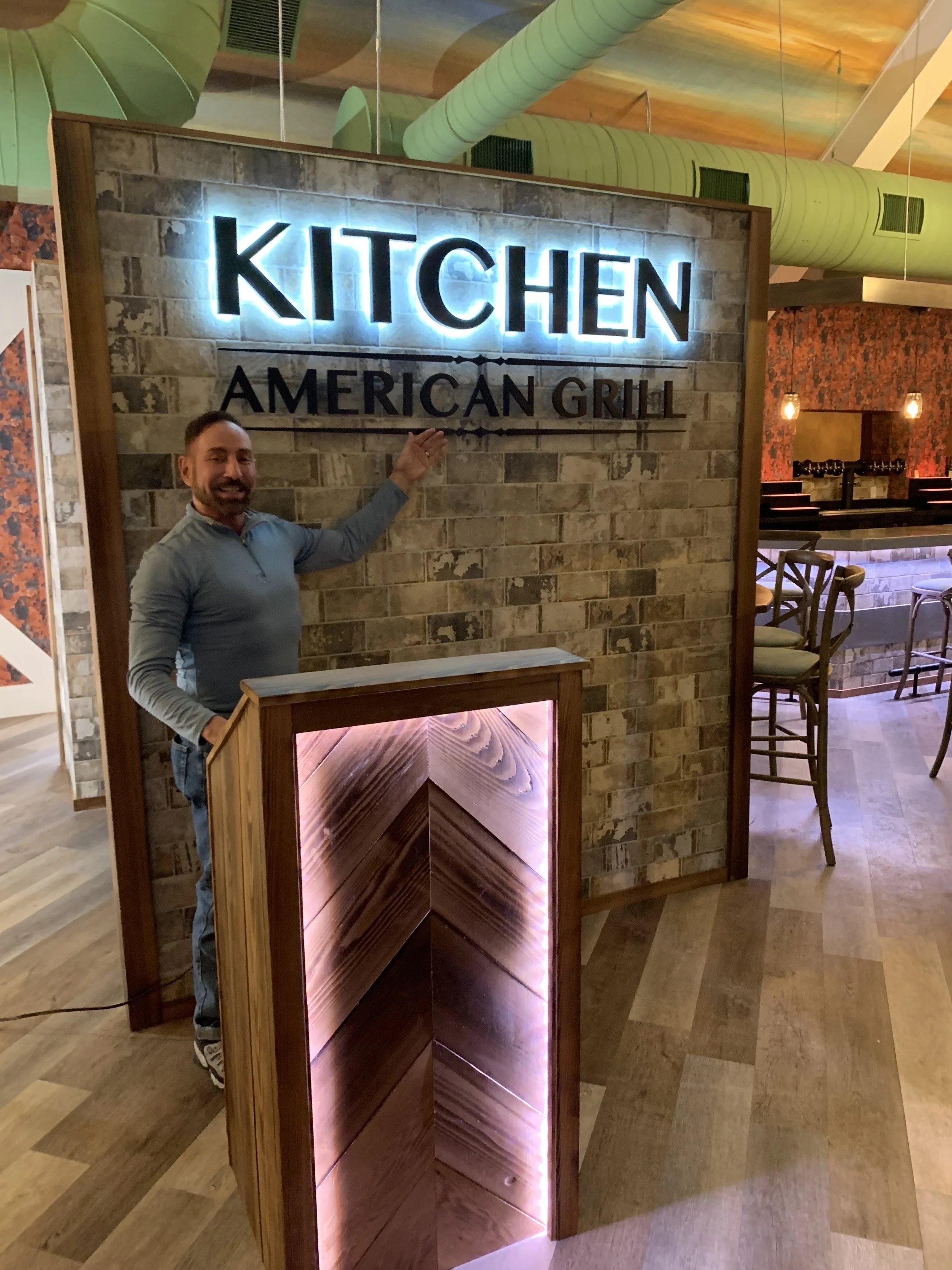 Designer Raymond Haldeman standing in front of the new back-lit Kitchen sign