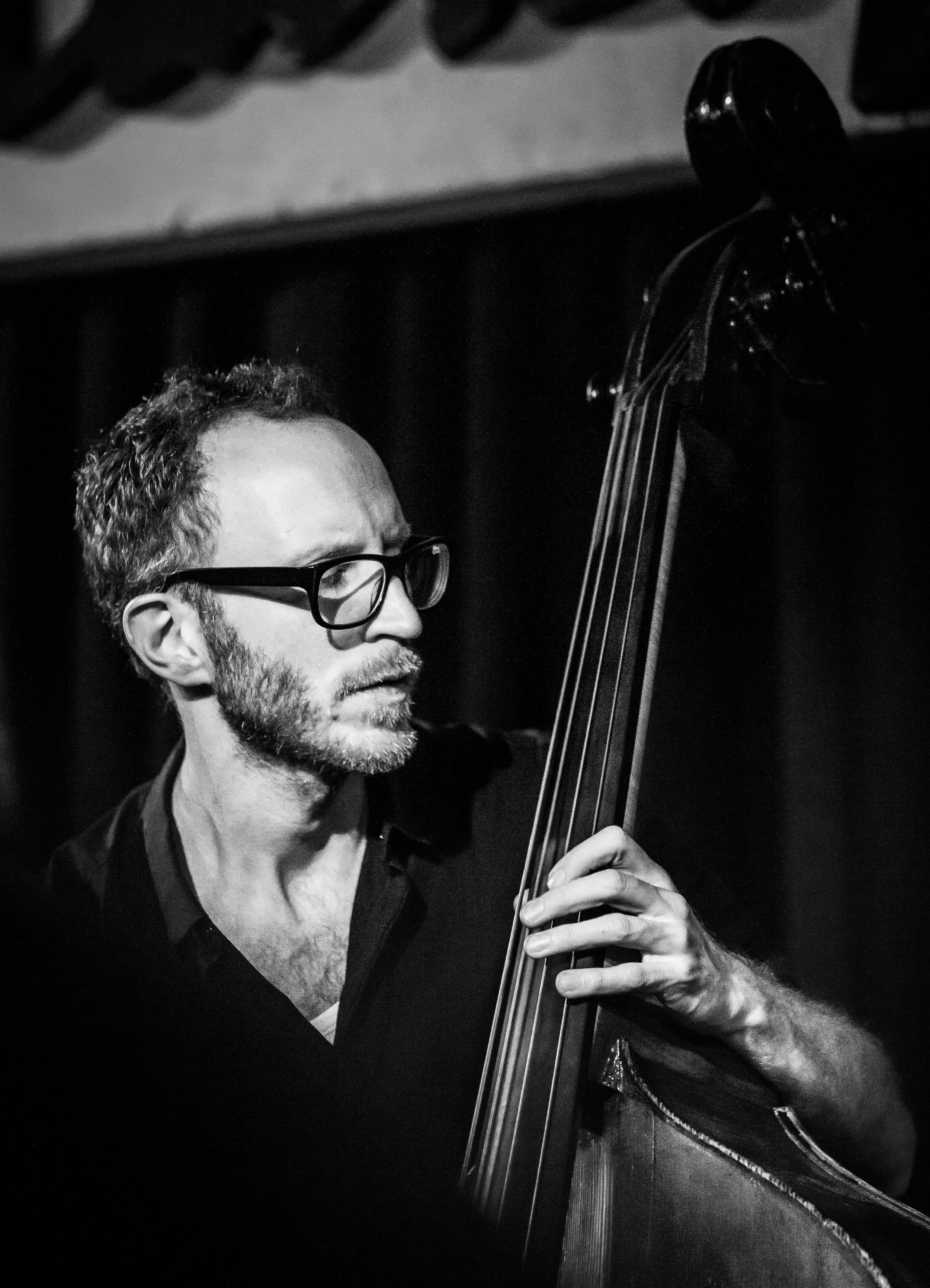 Black and white photo of a man with glasses playing a double bass.