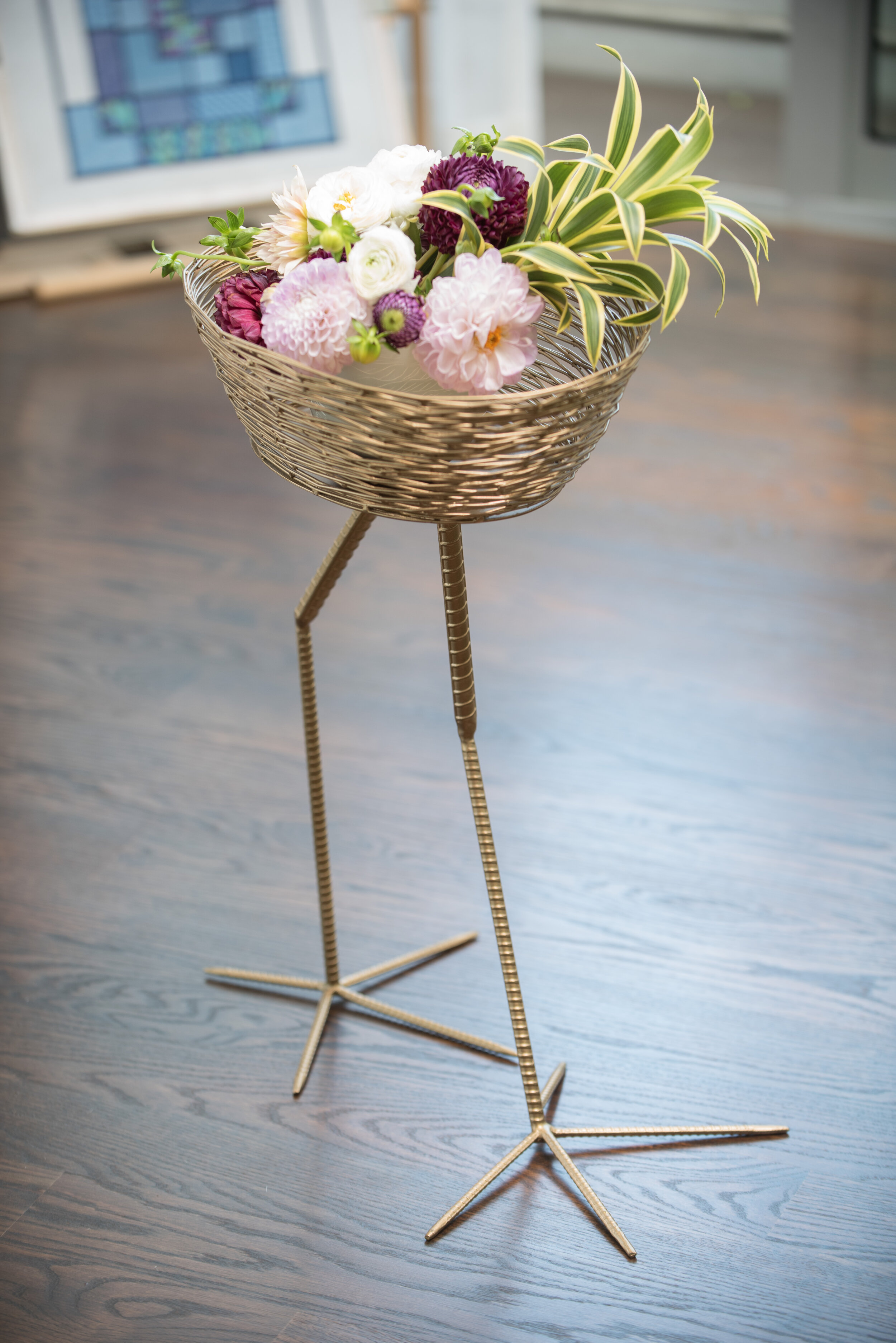 Scupltural woven gold basket on tall gold bird legs, holding pink, purple, and green flowers.