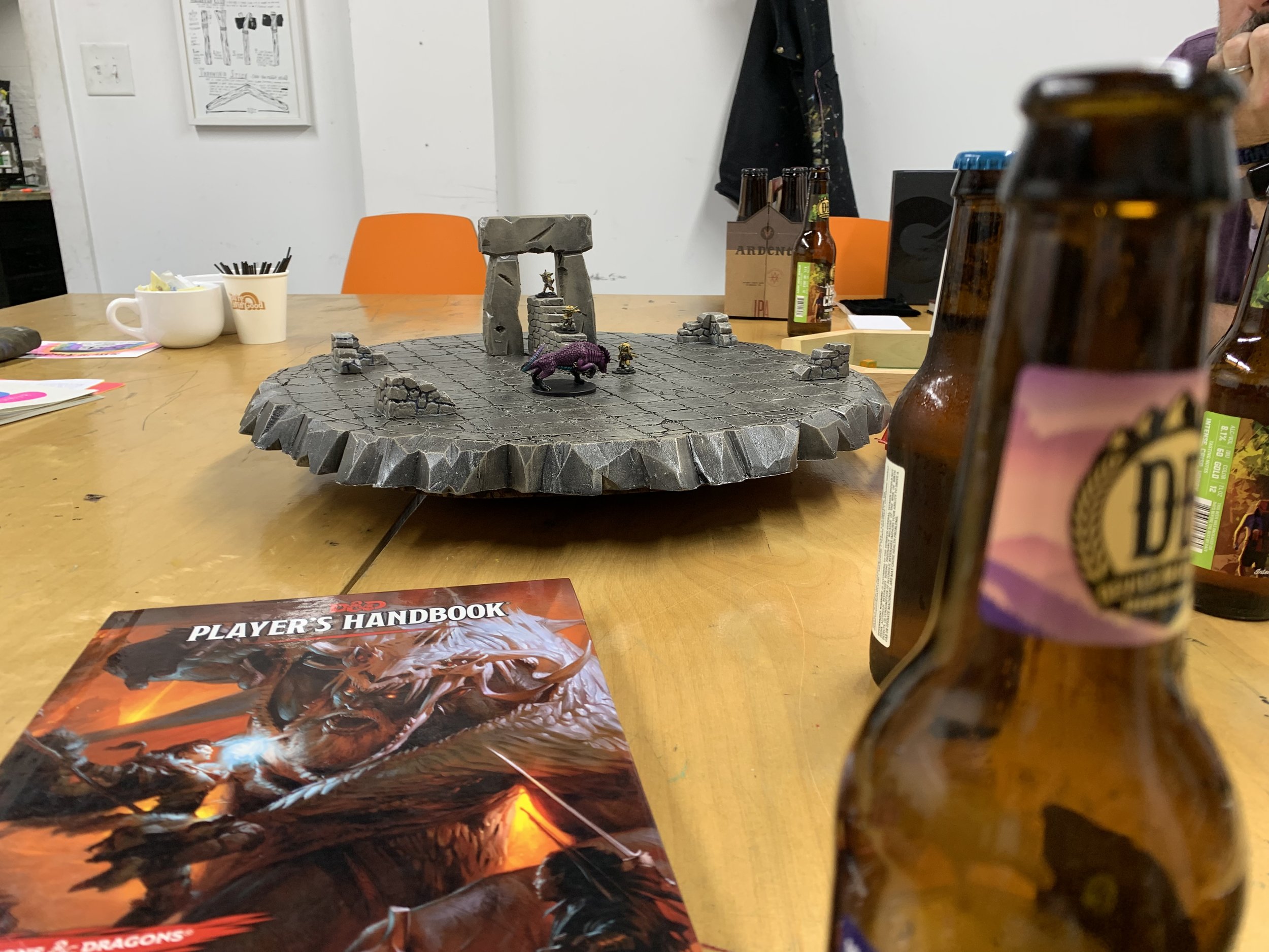 A picture of D&D miniatures and environment created by our friend Scott. There’s a Player’s Handbook and a beer bottle in the foreground.