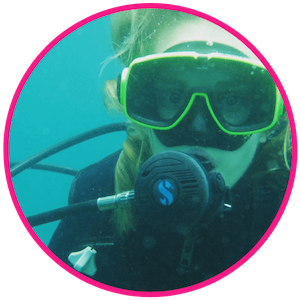 Melissa underwater scuba diving in full mask and reguator, her blonde hair waving in the water as she looks at the camera