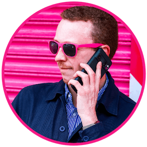 Headshot of Mark Grainger wearing bright pink rimmed shades whilst on a phone