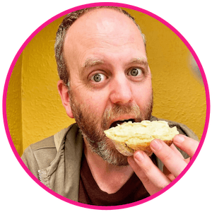 Headshot of Adrian looking at the camera whilst eating a cream scone