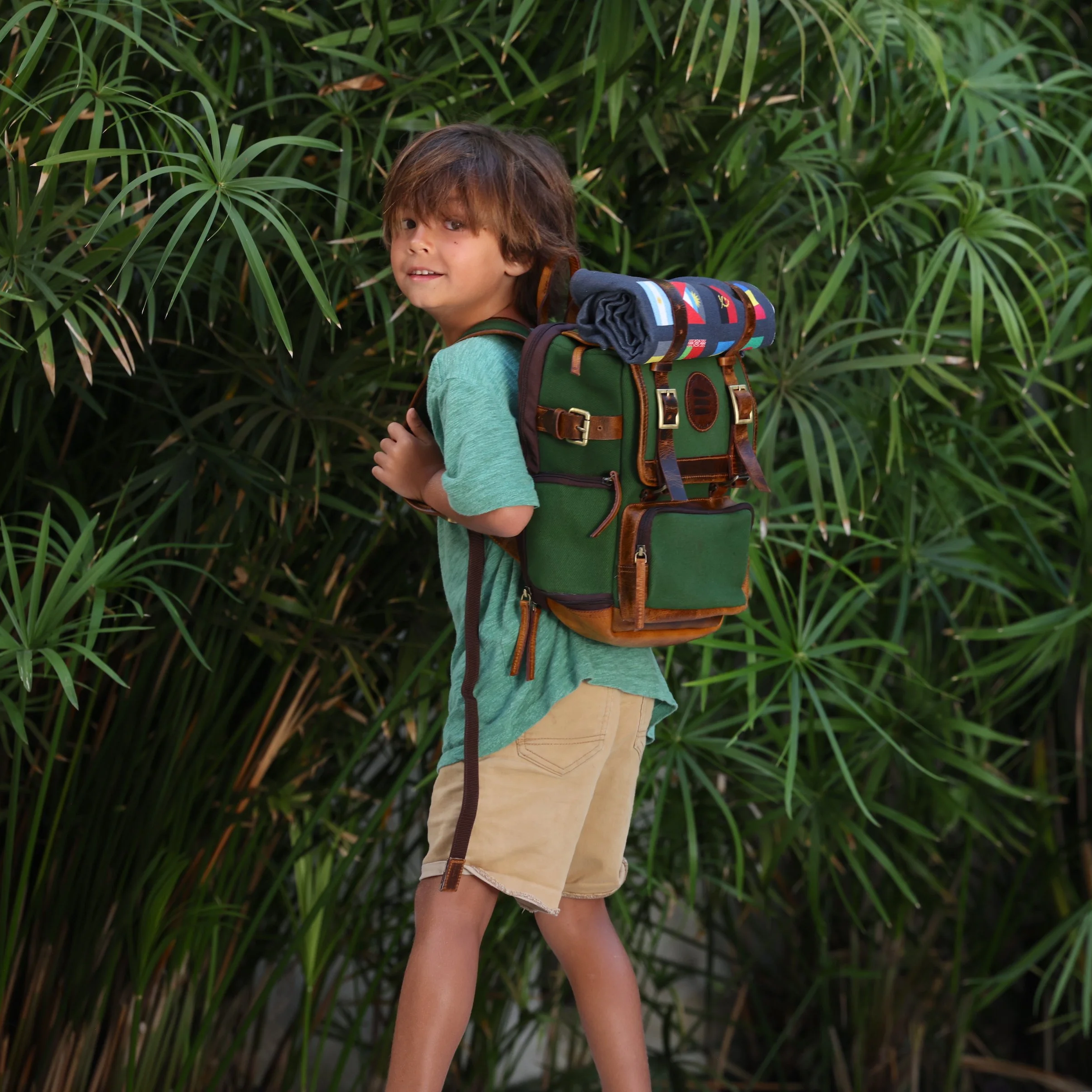 Young boy wearing a green backpack in front of plants