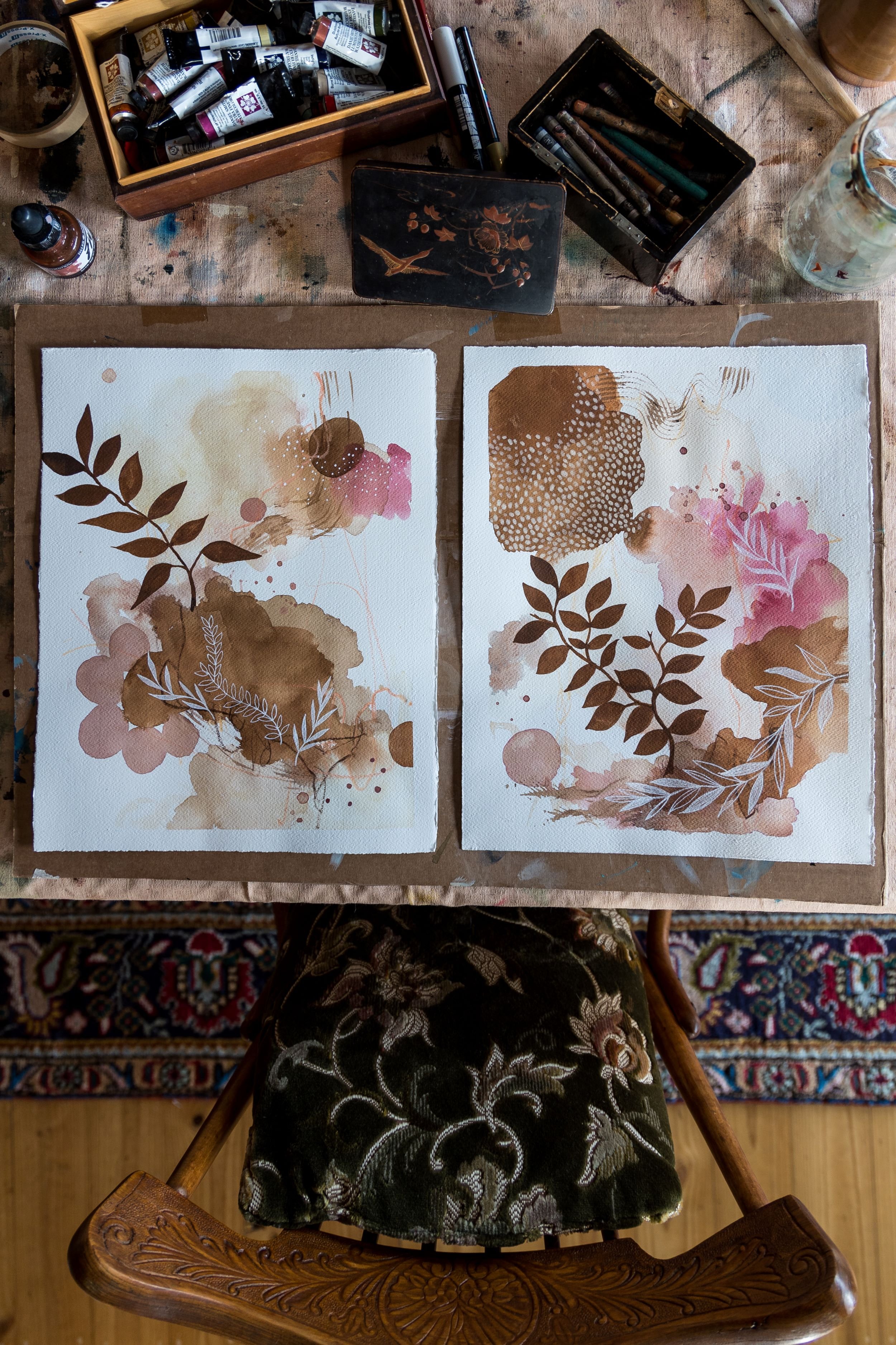  Bird’s eye view of artist Laura Horn’s table with two watercolour paintings on it. The paintings are close to completion.  
