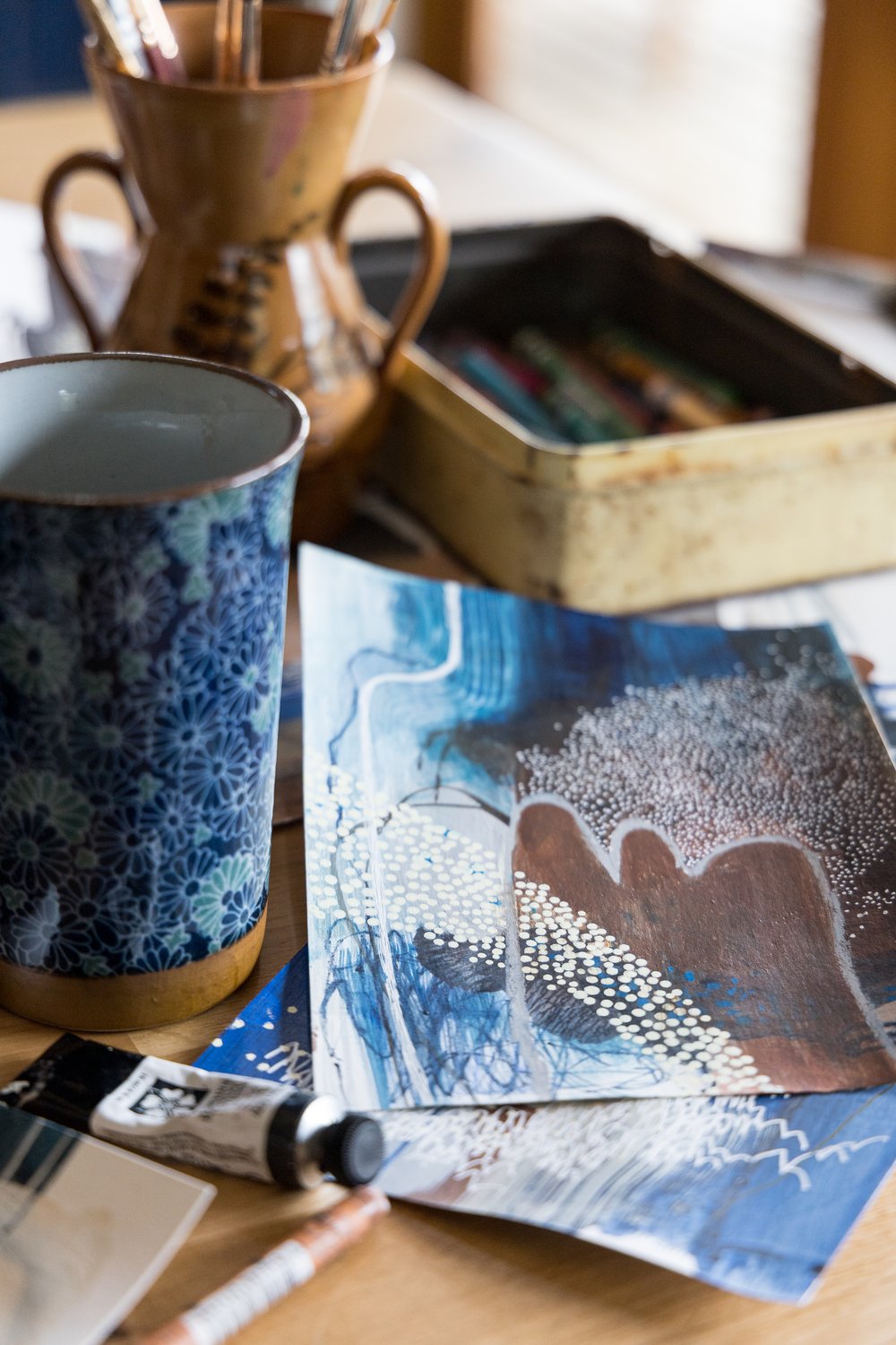  Close up photograph of abstract painting, art supplies, and tea mug.  