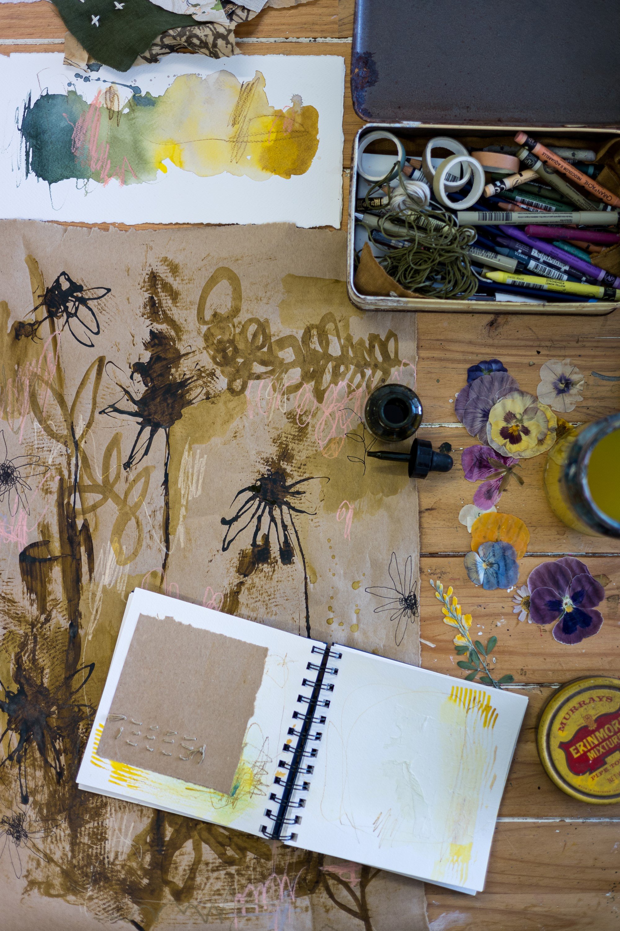  Piece of brown craft paper that has loose flowers painted on it with ink. The paper is surrounded by art supplies.  