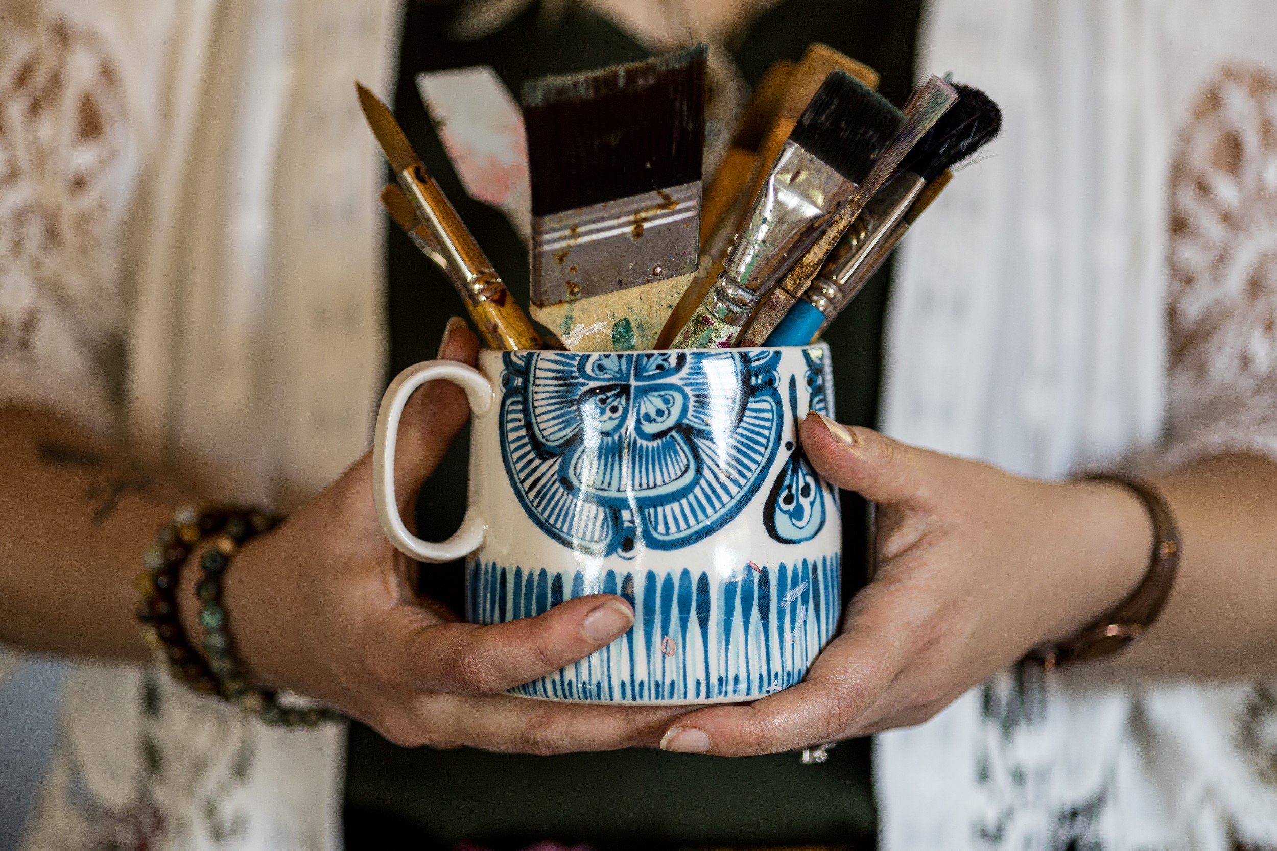  A mug containing various mixed media paint brushes. The mug is being held by two hands. 