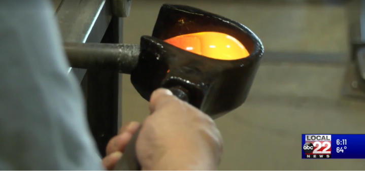 A person holding a pot with a bright orange hot piece of metal inside, in a forge or metalworking setting.