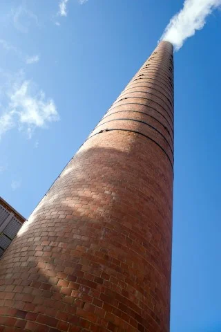 a-tall-brick-factory-smoke-stack-billowing-with-steam-and-smoke_SKLelwLCBj.jpg