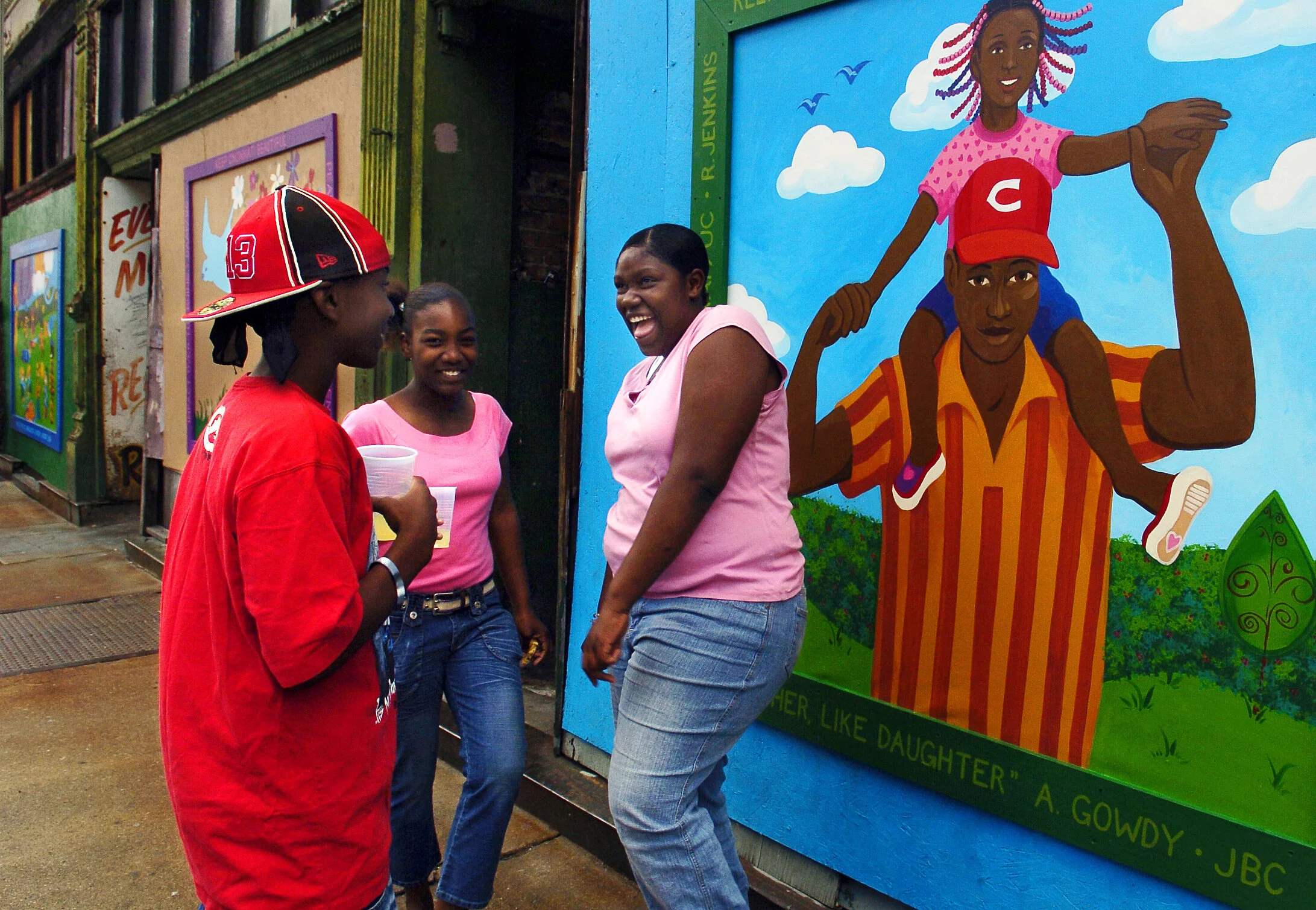 Tirai Gill, left, Jasmine Murray, center, and Rishina Jenkins, right, pass by the new murals added to blighted buildings on Vine St. in Cincinnati, Thursday, June 16, 2005.