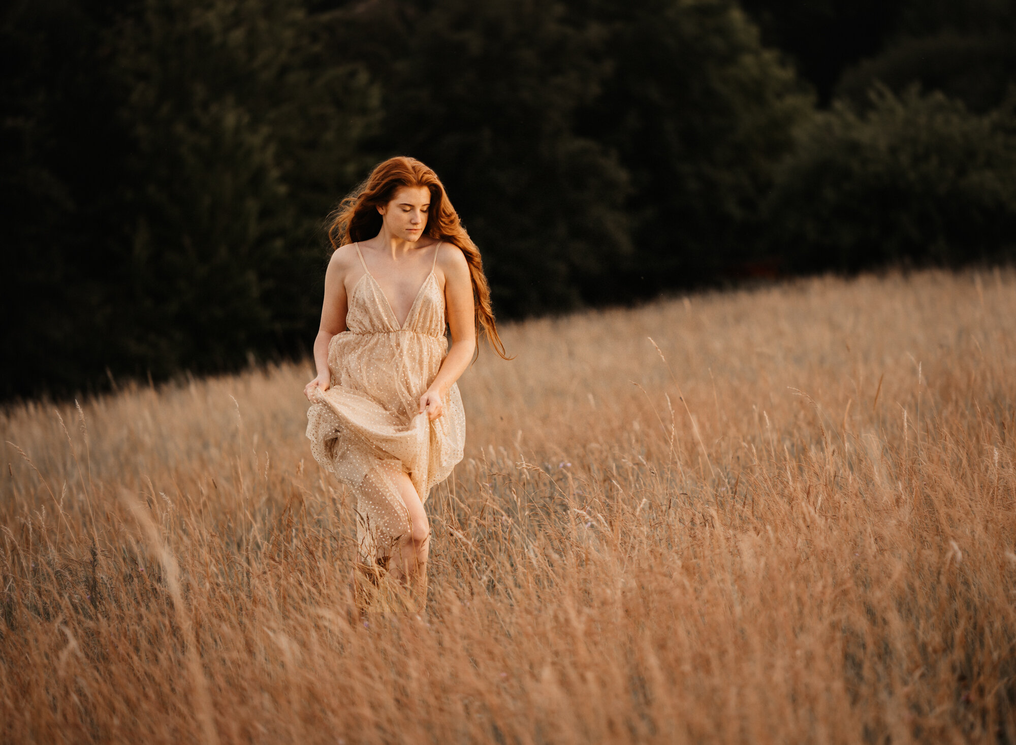  Young red head girl wearing a gold sparkling dress in a wild flower field in summer during sunset for her fine art portrait photo session by ramstein kmc photographer sarah havens, Kaiserslautern Germany - running through the field   