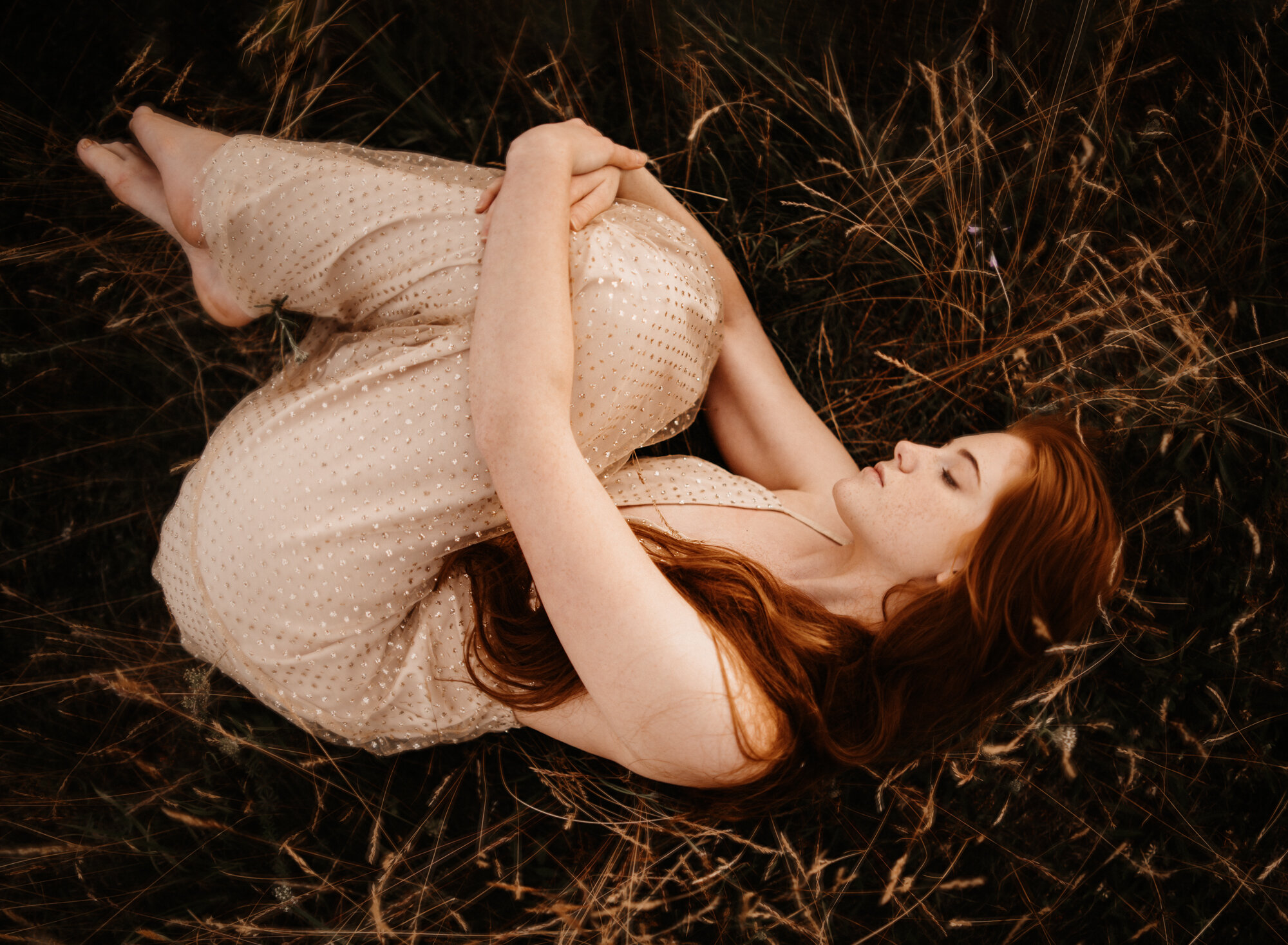  Young red head girl wearing a gold sparkling dress in a wild flower field in summer during sunset for her fine art portrait photo session by ramstein kmc photographer sarah havens, Kaiserslautern Germany 