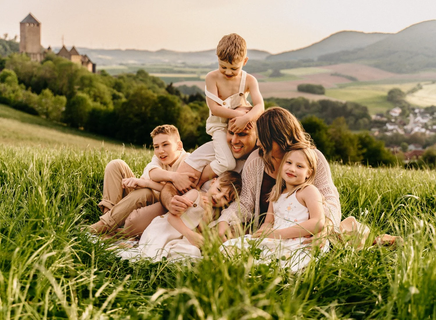 Family sitting in a grassy field with distant hills and a castle visible.