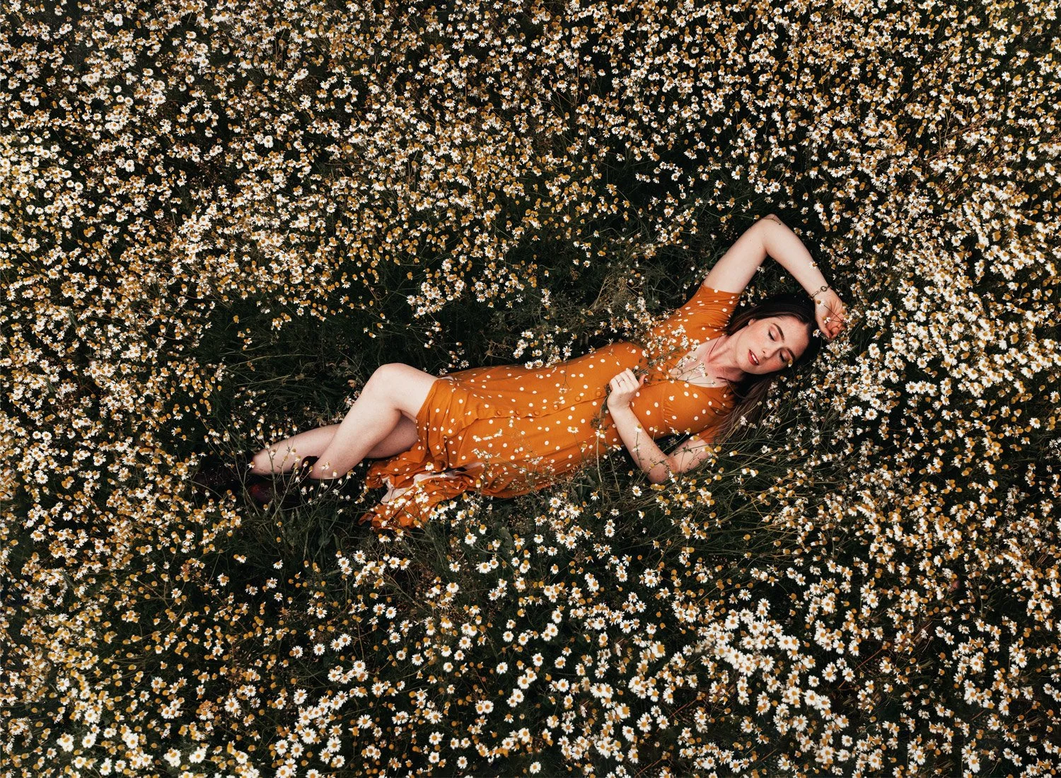 Woman in orange dress lying in daisy field