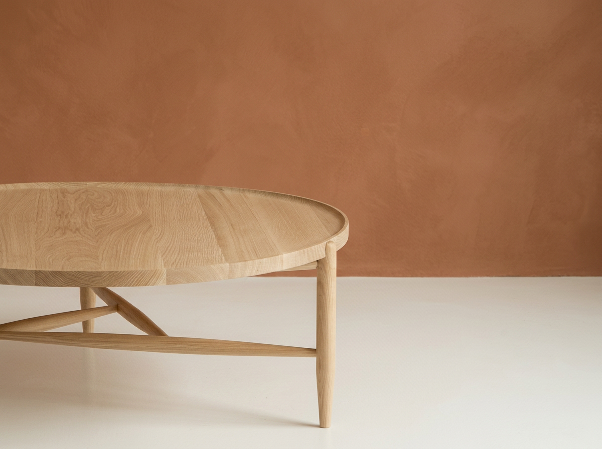 Part of a round wooden table with a natural finish, set against a reddish-brown wall and white flooring.