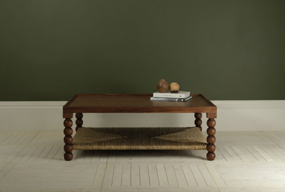 Wooden table with books and decorative pottery on top, set against a green wall with white baseboard and light hardwood flooring.